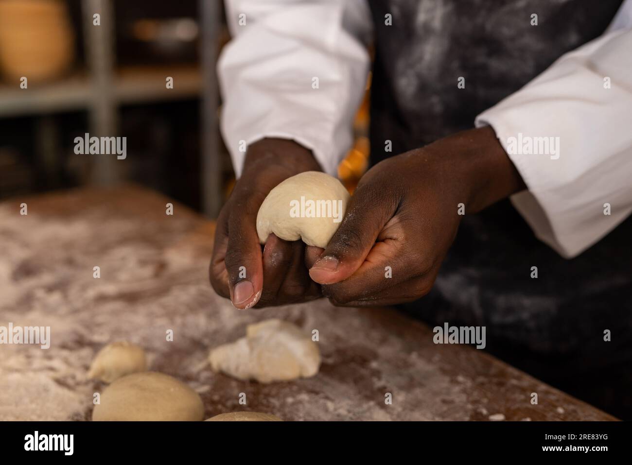 Boulanger mâle afro-américain dans la cuisine de boulangerie formant la pâte pour les rouleaux Banque D'Images