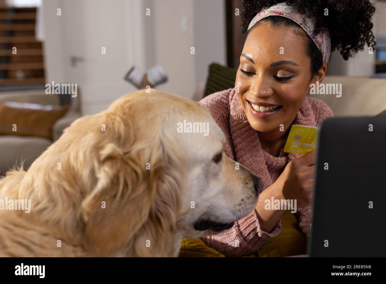 Heureuse femme biracial utilisant un ordinateur portable et caressant un chien à la maison Banque D'Images