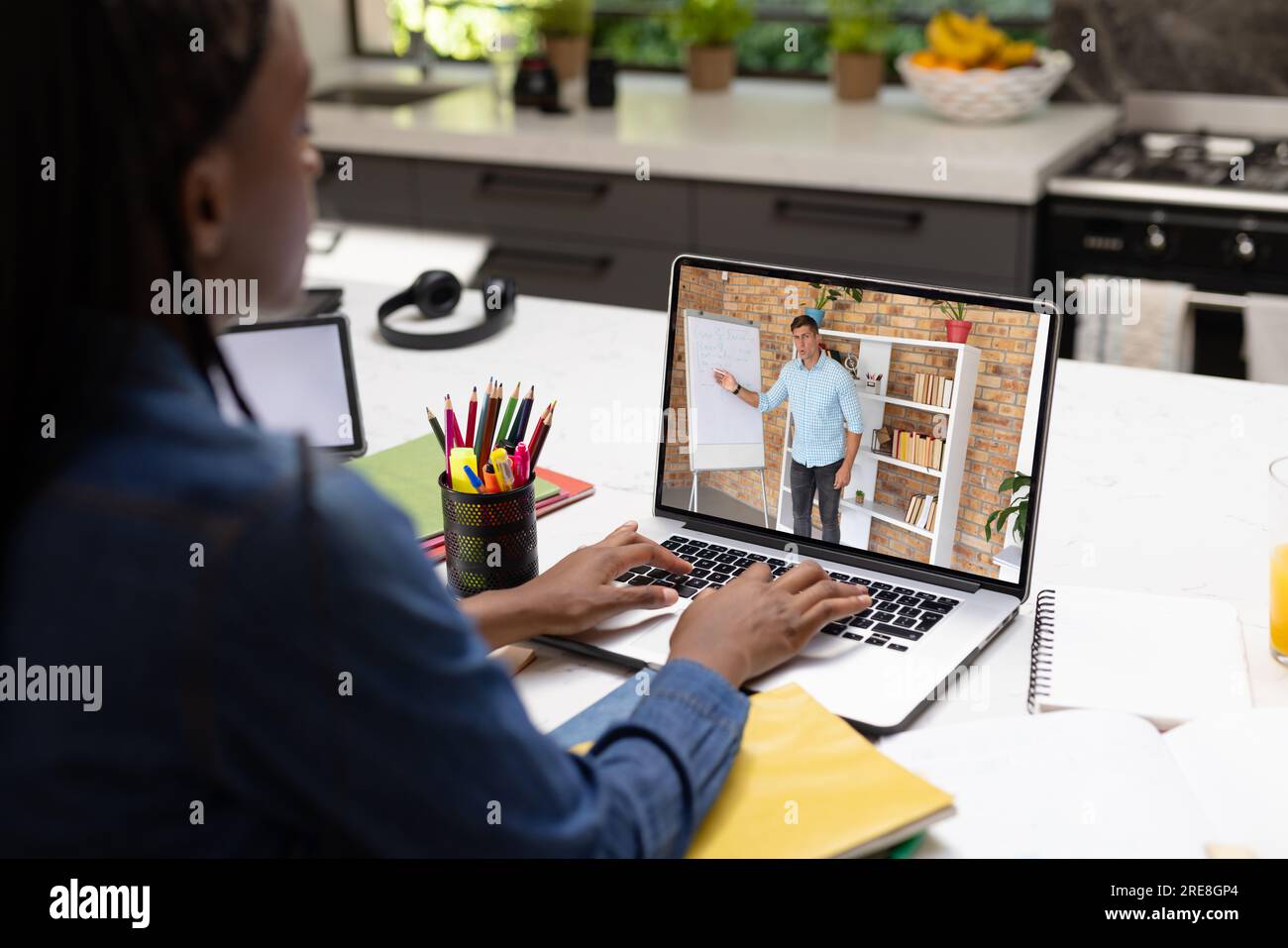 Vue arrière d'une écolière afro-américaine ayant un appel vidéo avec un professeur masculin sur ordinateur portable Banque D'Images