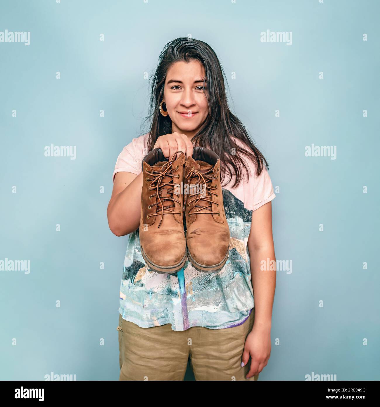 Une femme aux cheveux noirs tient une paire de chaussures. Femme hispanique montrant des chaussures usées. Banque D'Images