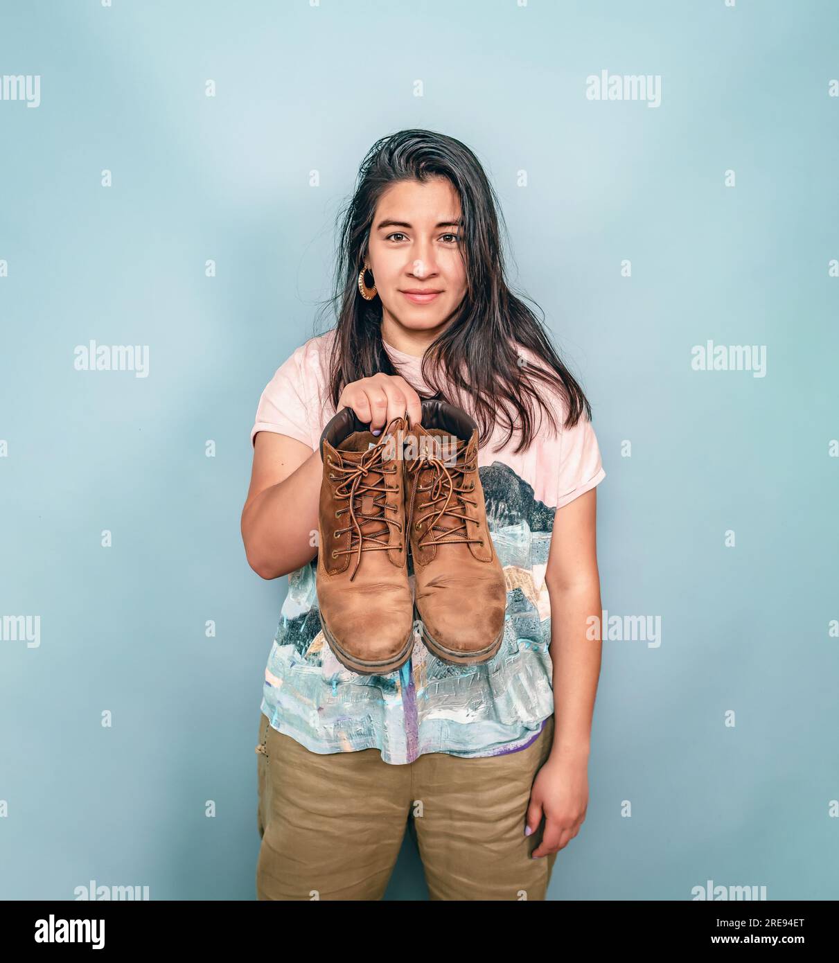 Une femme aux cheveux noirs tient une paire de chaussures. Femme hispanique montrant des chaussures usées. Banque D'Images