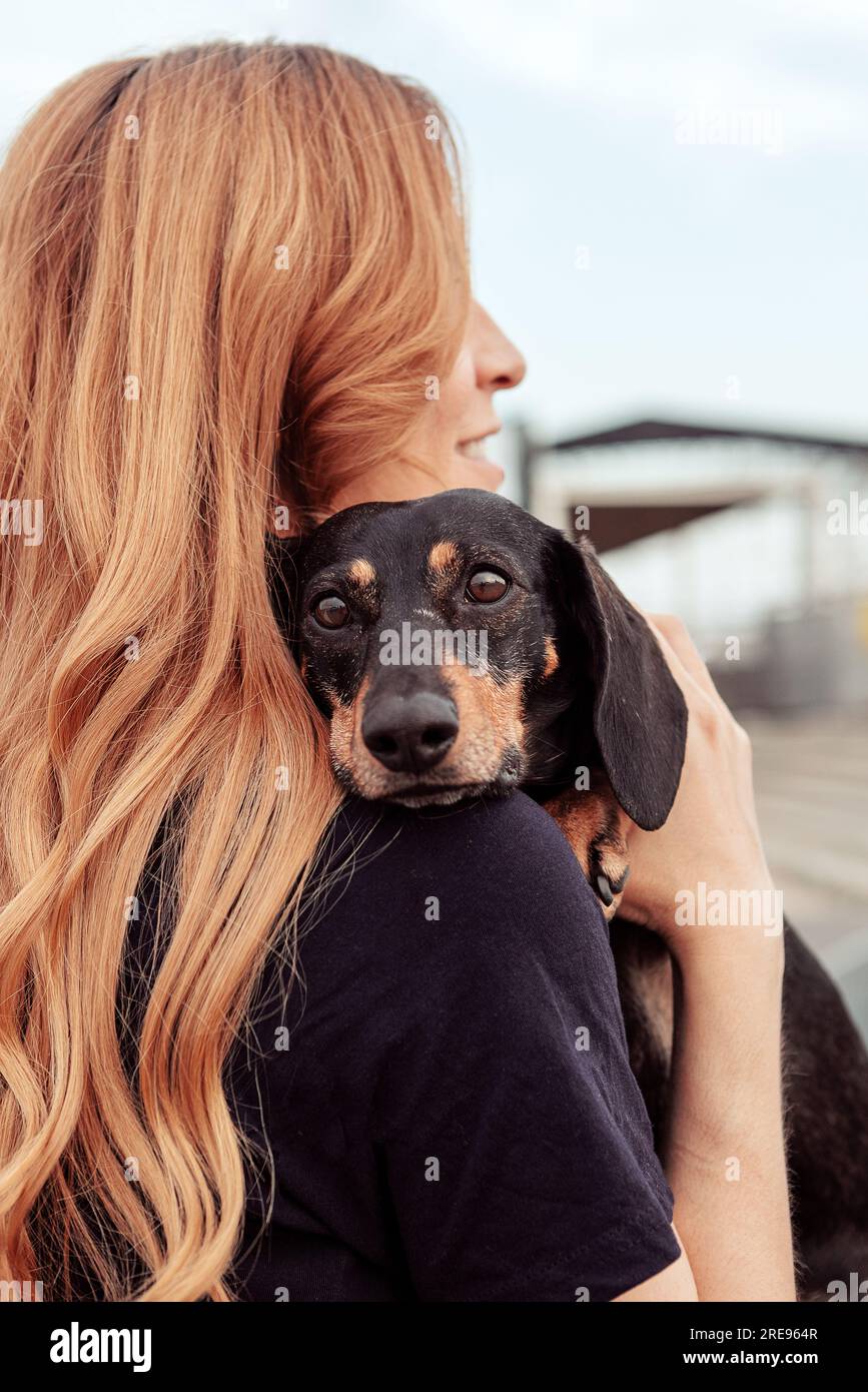 Vue latérale de la femme rousse embrassant le chien Teckel tout en marchant dans la rue ensemble pendant le week-end Banque D'Images