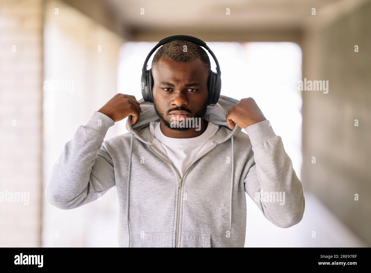 Portrait de jeune homme barbu afro-américain en vêtements de sport regardant la caméra tout en se tenant debout avec le casque dans votre oreille et touchant le capot de ja Banque D'Images