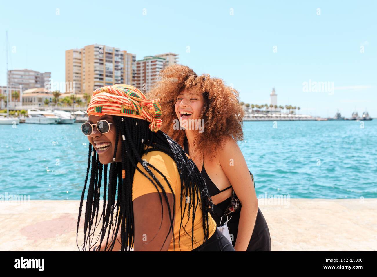 Groupe de diverses femelles soulevant des amis tout en riant et debout en bord de mer en été pendant la promenade de la ville Banque D'Images