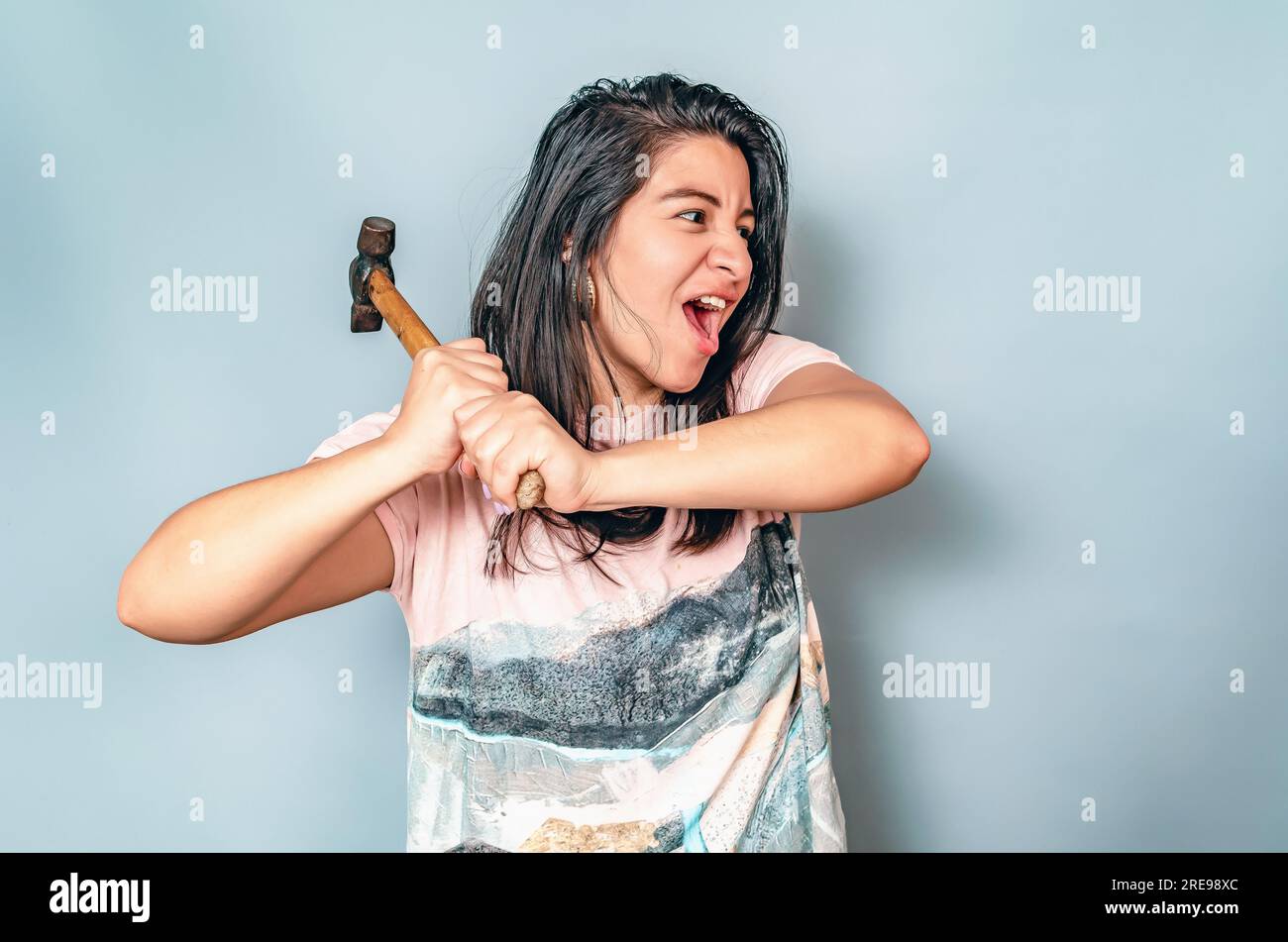 Vue de côté femme en chemise blanche balance le marteau. Femme agressive avec un marteau. Hispanique Banque D'Images