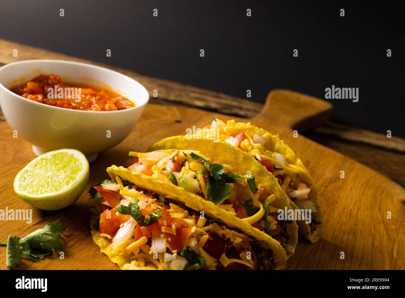 Vue à angle élevé des tacos au citron, coriandre et sauce dans un bol sur la planche de service au-dessus d'une table en bois Banque D'Images Vue à angle élevé des tacos au citron, coriandre et sauce dans un bol sur la planche de service au-dessus d'une table en bois Banque D'Images