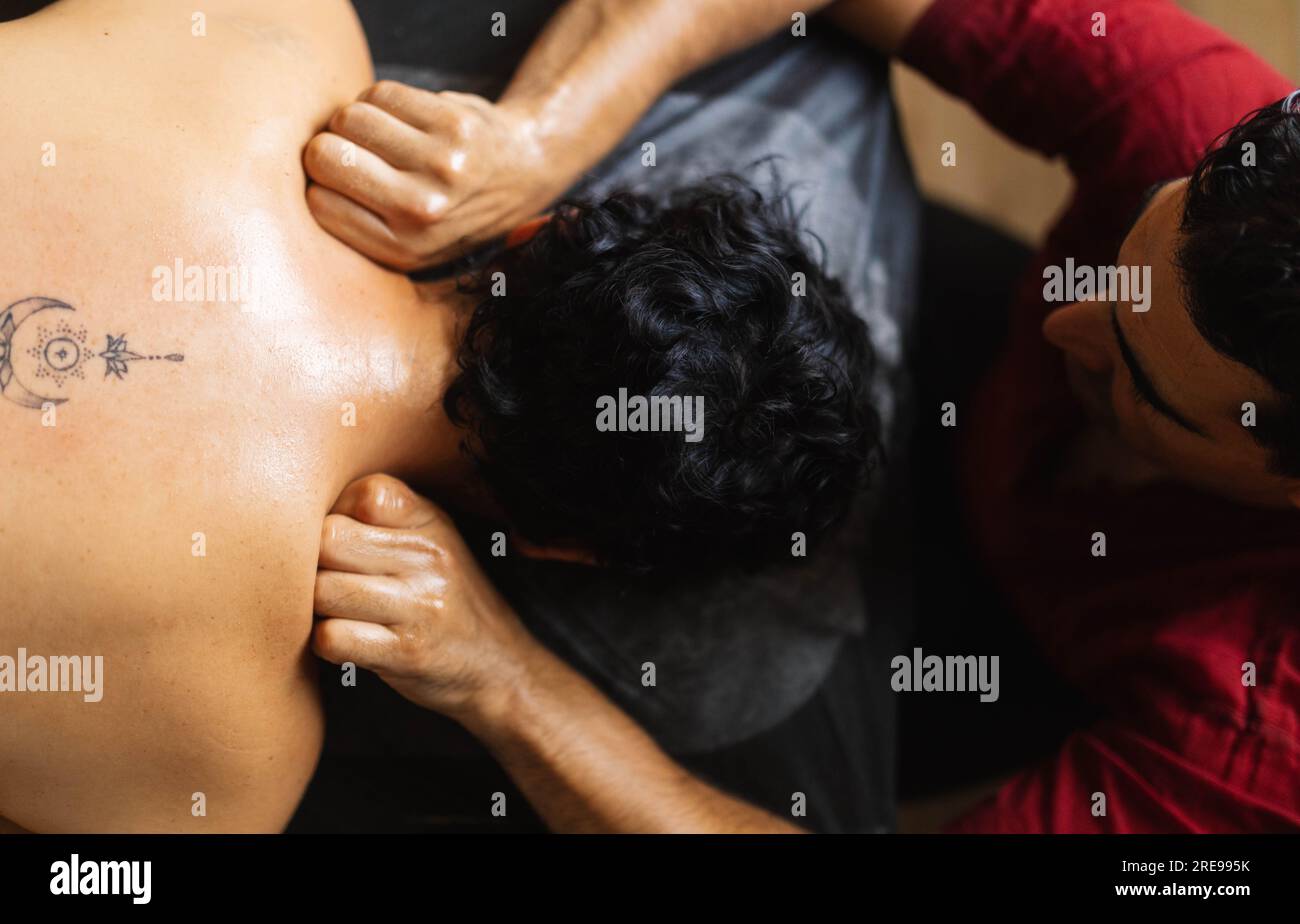 Vue de dessus d'un thérapeute masculin debout au bureau et effectuant le pétrissage des épaules avec les doigts pliés sur une cliente féminine anonyme Banque D'Images