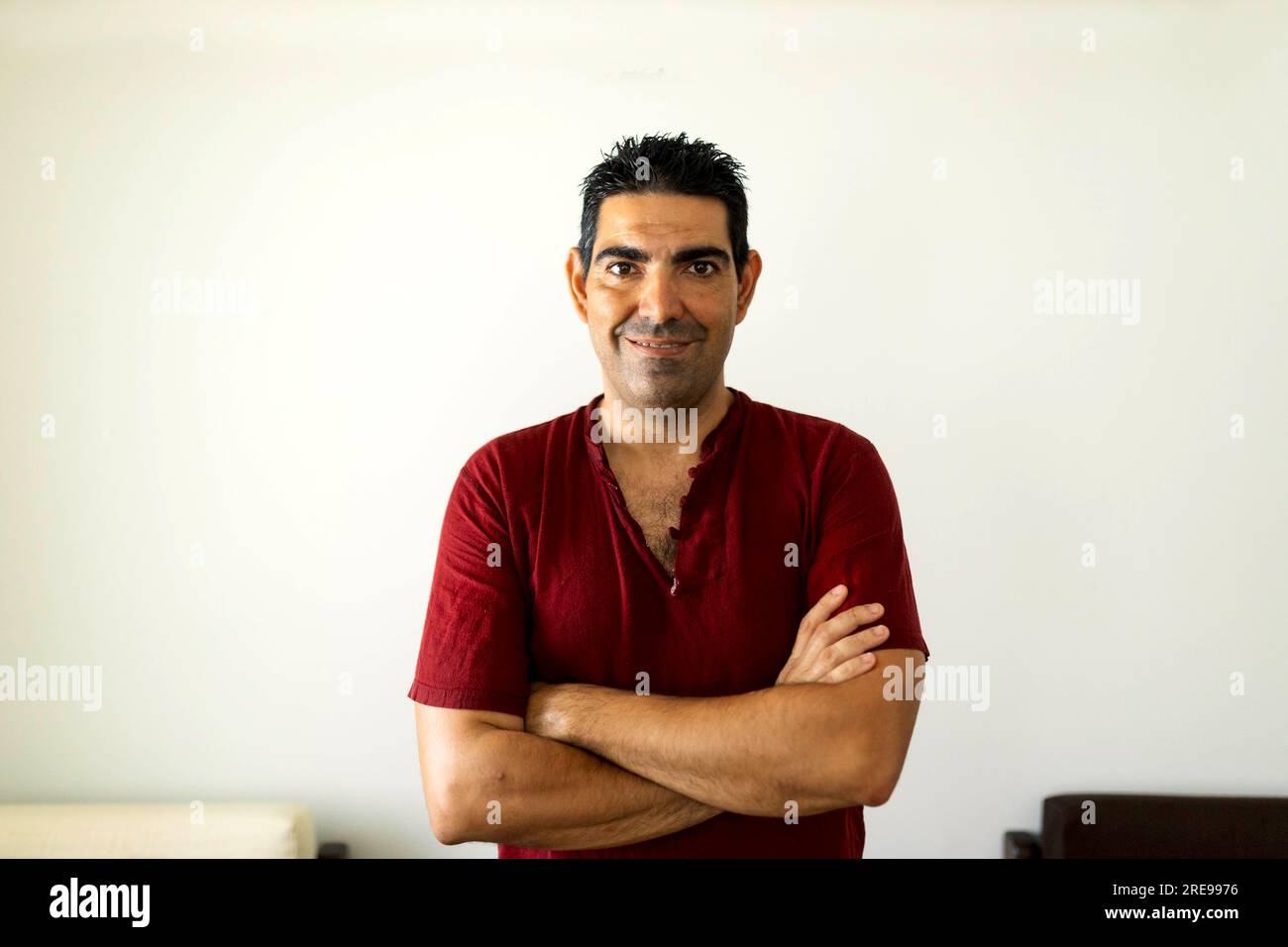 Portrait de thérapeute hispanique adulte souriant avec les mains croisées regardant la caméra tout en se tenant dans la lumière du jour pendant la pause des massages dans le salon Banque D'Images