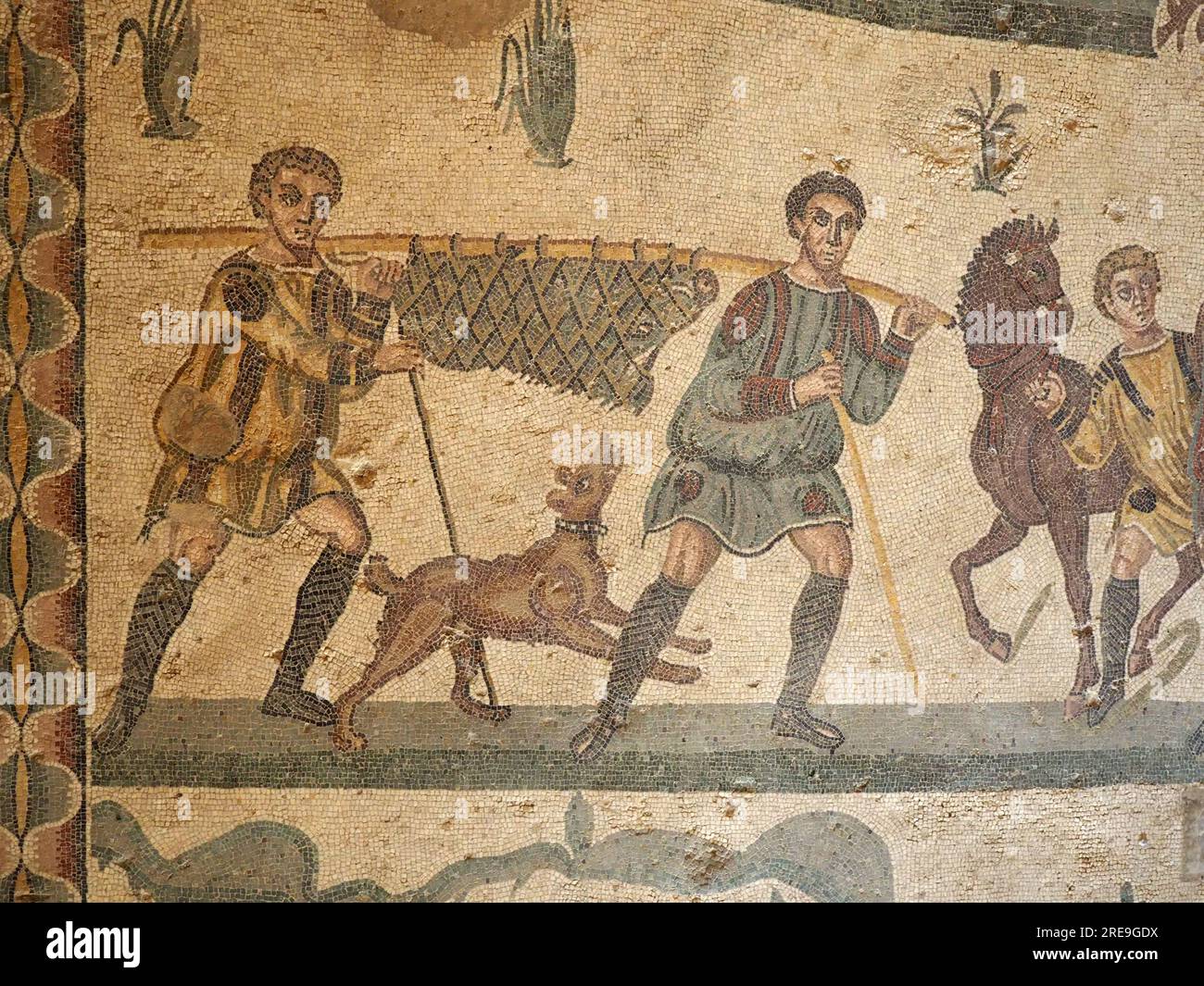 Mosaïque dans la salle de la petite chasse, Villa Romana del Casale, Sicile, représente deux hommes avec un chien de chasse portant un sanglier en ferme sur un poteau. Banque D'Images