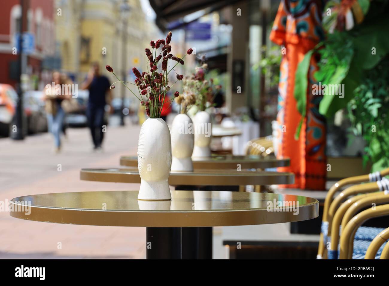 Café de rue dans la ville avec des tables vides en plein air sur fond de personnes marchant. Vases de fleurs sur des tables rondes et des chaises confortables Banque D'Images
