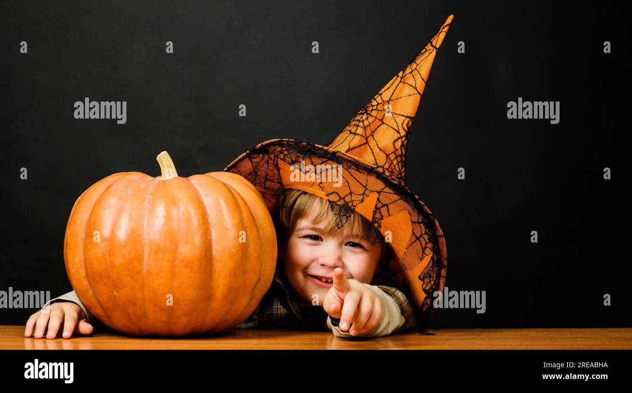 Garçon souriant dans le chapeau de sorcière avec la citrouille halloween pointant vers vous. Trick ou Treat. Petit enfant avec citrouille. Préparation pour les vacances d'Halloween. Heureux Banque D'Images