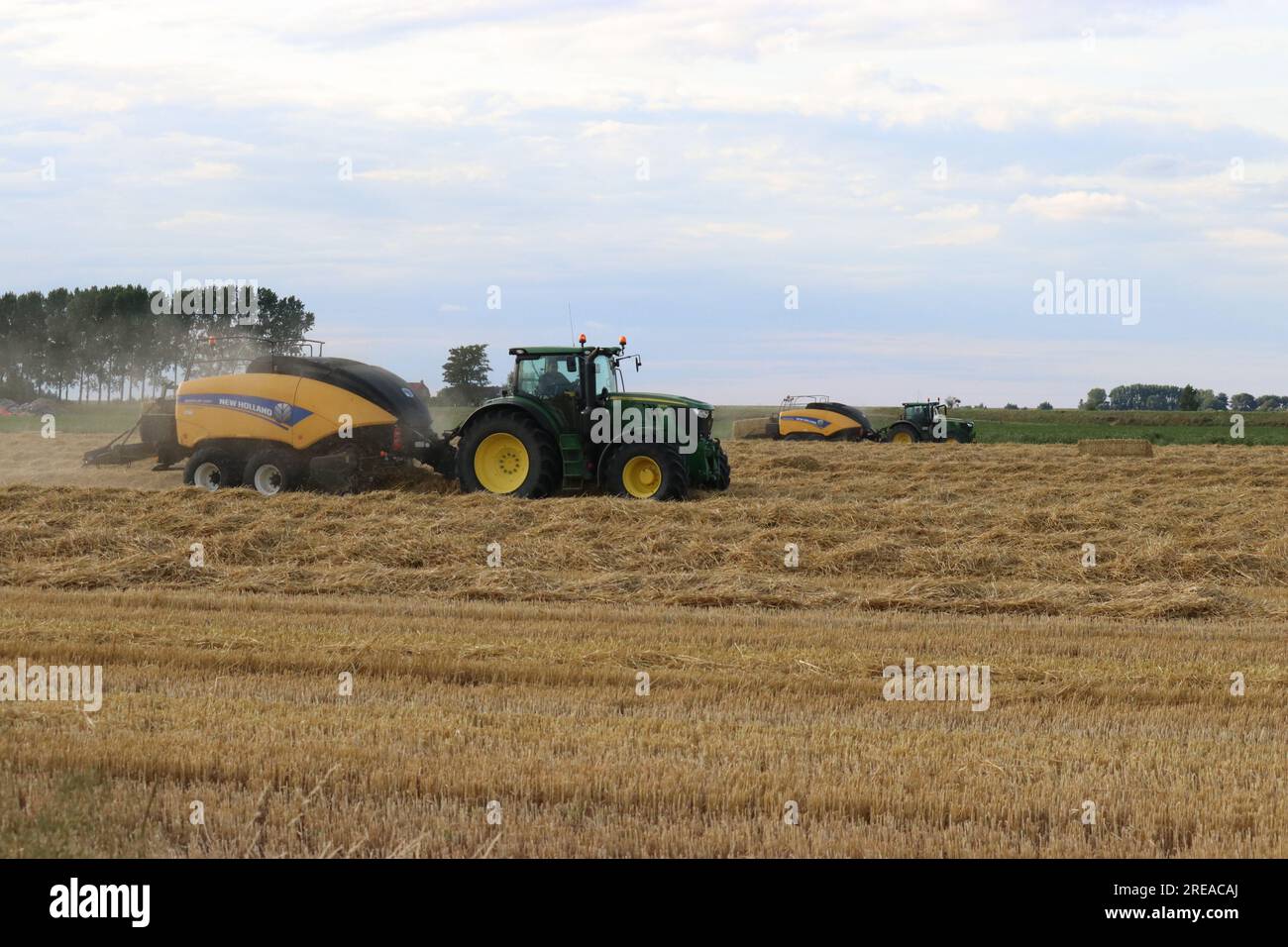 un paysage rural avec deux tracteurs et une grande presse à balles dans un champ jaune avec des rangées de paille faisant des balles de foin dans la campagne néerlandaise en été Banque D'Images