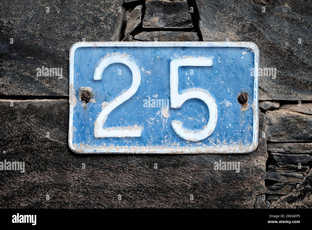 Numéro 25, vingt-cinq, sur une plaque bleue sur un fond de mur de pierre. Banque D'Images