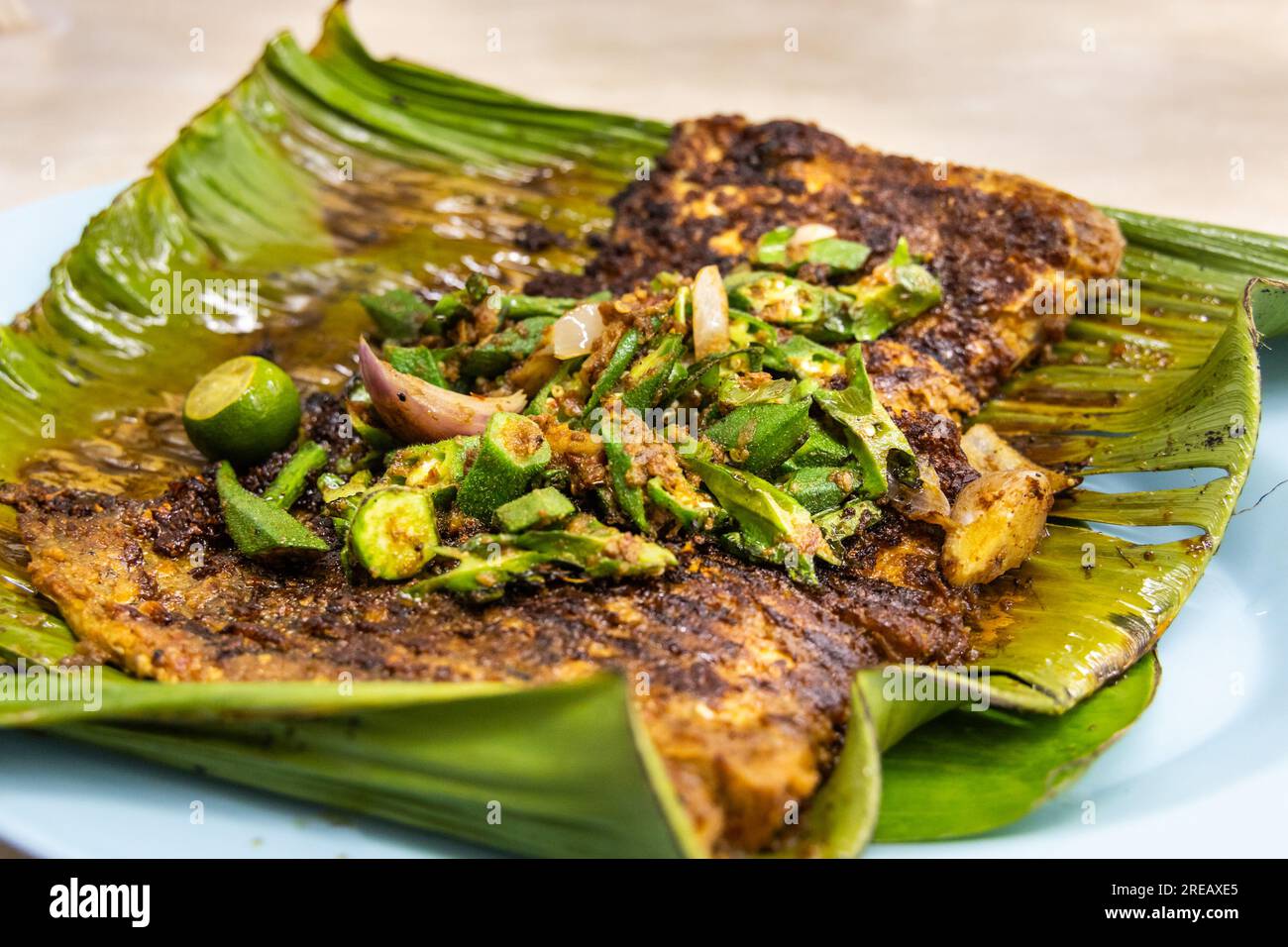 Gros plan de poissons raies grillés aux épices garnis de légumes d'okra sur des feuilles de bananier, plats populaires en Malaisie Banque D'Images