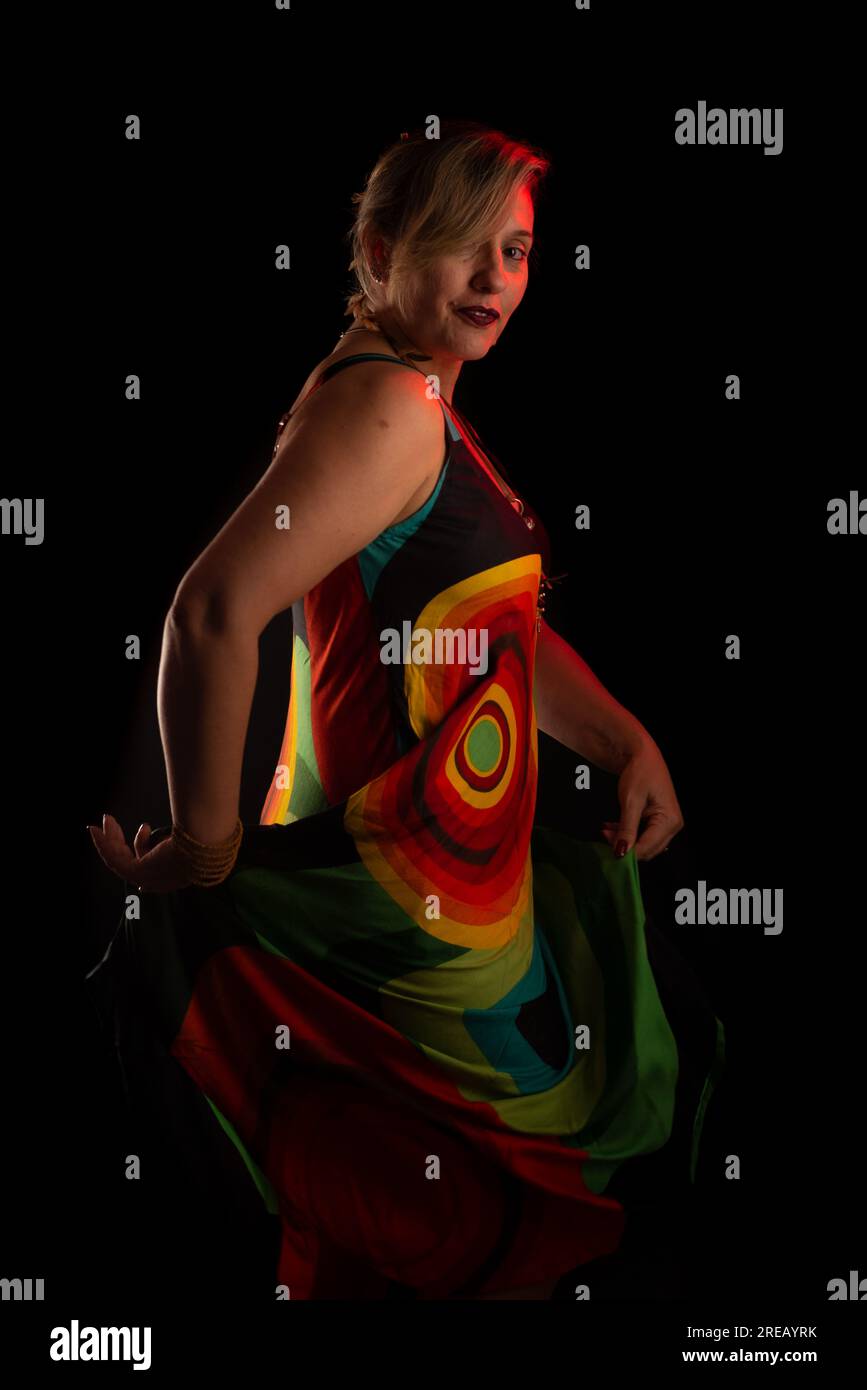 Belle femme caucasienne debout portant une robe colorée. Portrait de studio. Isolé sur un fond noir. Banque D'Images