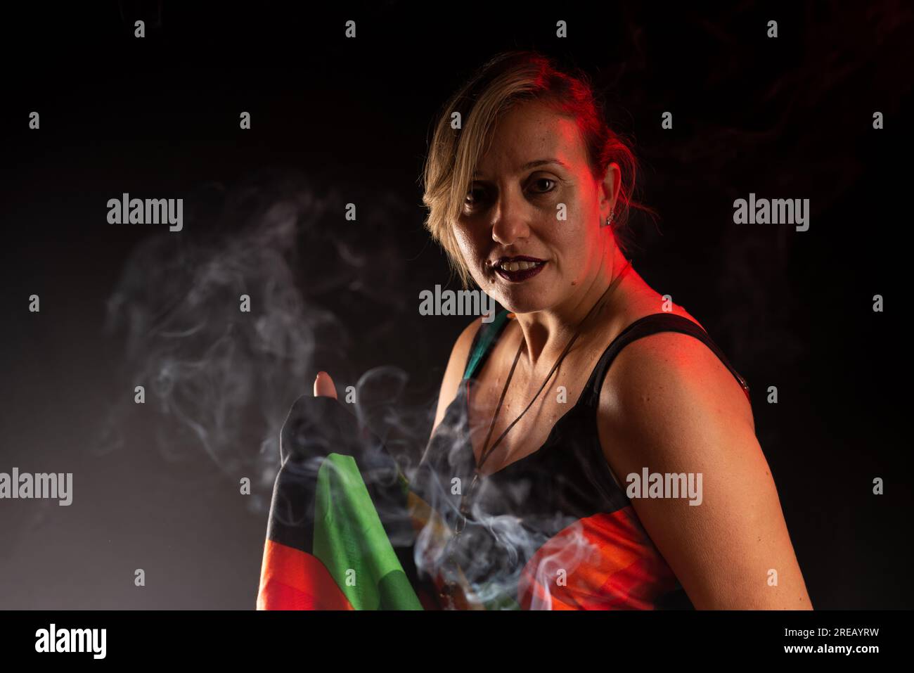 Femme caucasienne attrayante debout, tenue de robe colorée. Portrait de studio. Fumée d'Encens tout autour. Isolé sur un fond noir. Banque D'Images