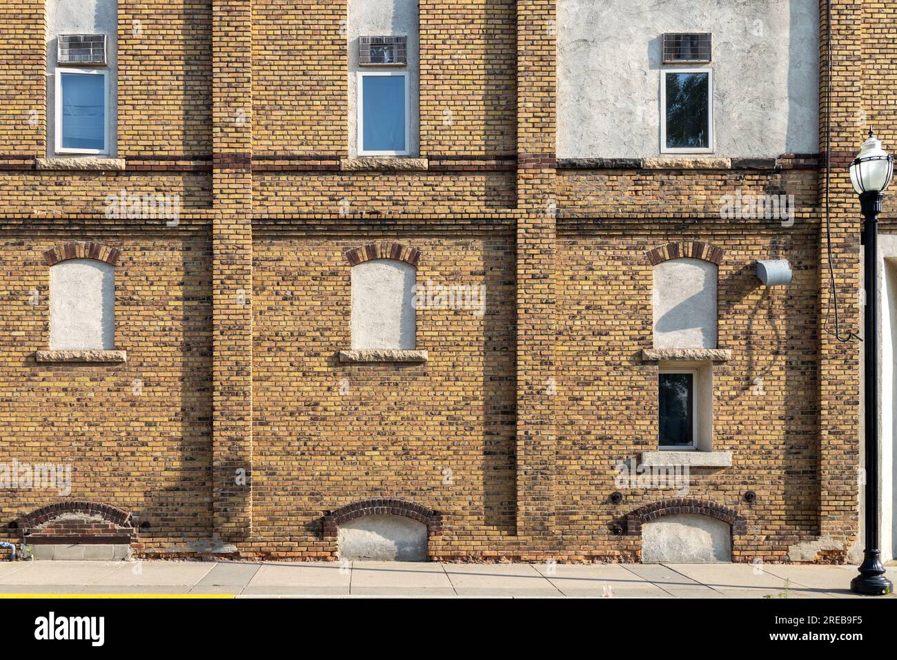 Fond de texture d'une vieille façade de bâtiment en briques jaunes et brunes avec vue sur les fenêtres cintrées fermées sur une rue urbaine Banque D'Images