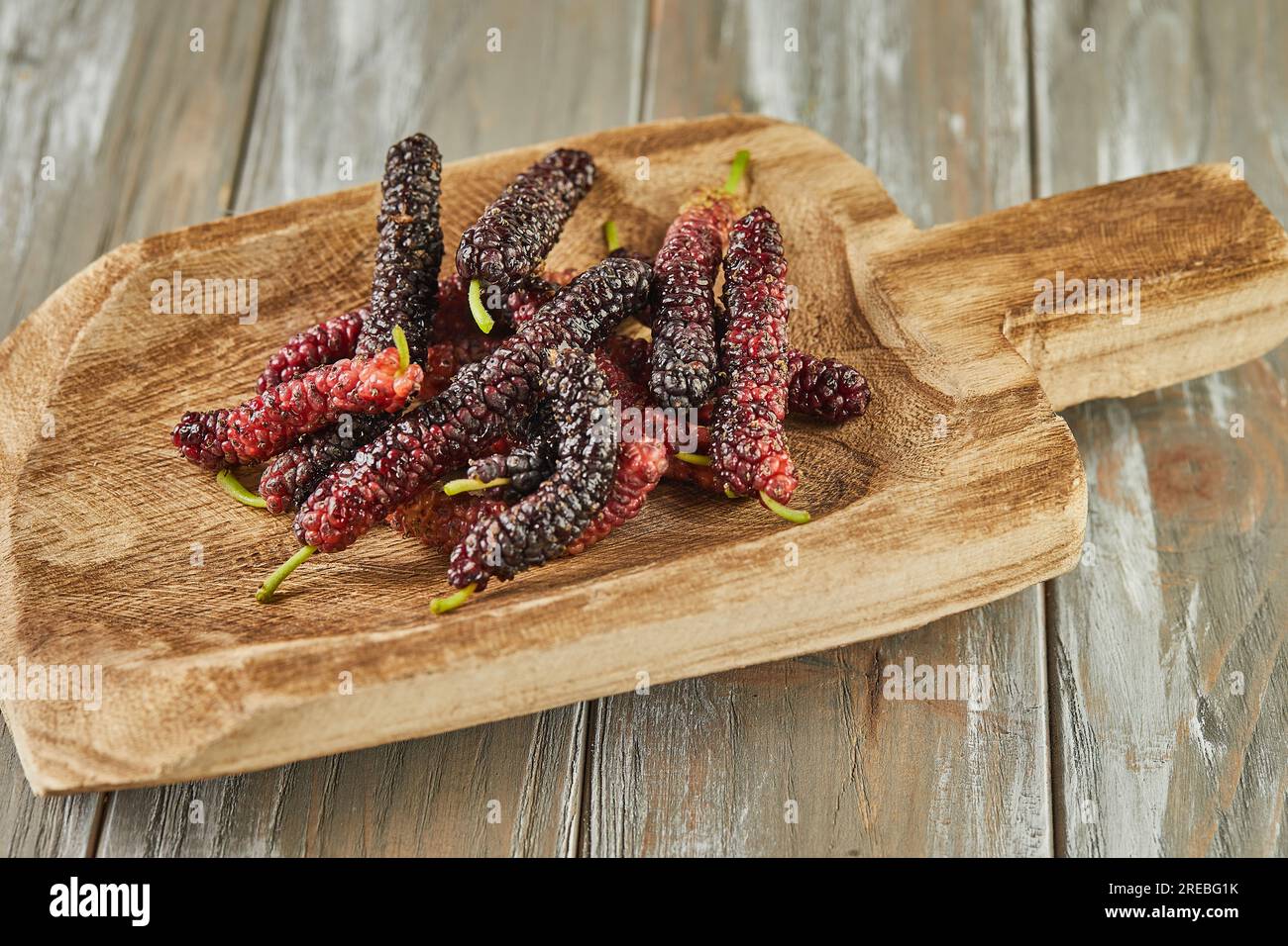 Mûrier afghan noir et rouge sur pelle en bois sur fond en bois gris. Banque D'Images