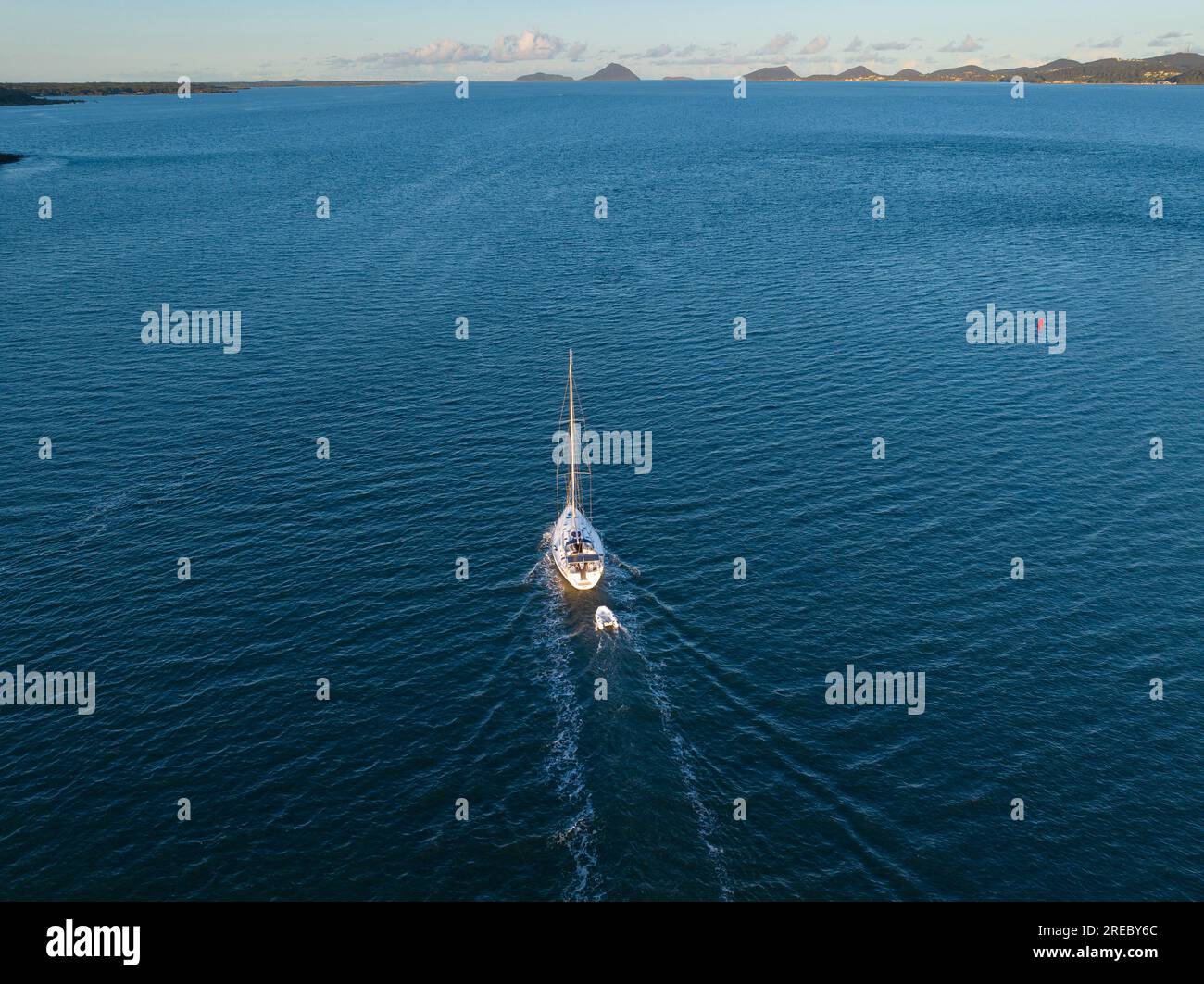 Un yacht solitaire remorquant un petit canot sur un large océan bleu à Soldiers point en Nouvelle-Galles du Sud, en Australie Banque D'Images