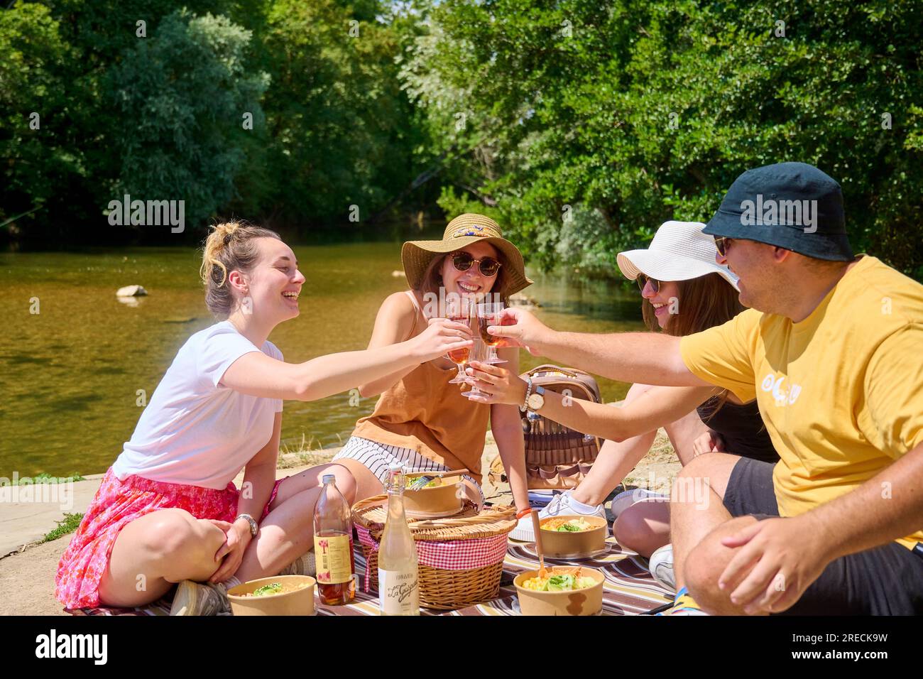 Pique-nique au bord du Doubs et du Canal Charles Quint à Dole (nord-est de la France) : groupe d'amis déjeunant au bord de l'eau en été, avec casquettes Banque D'Images