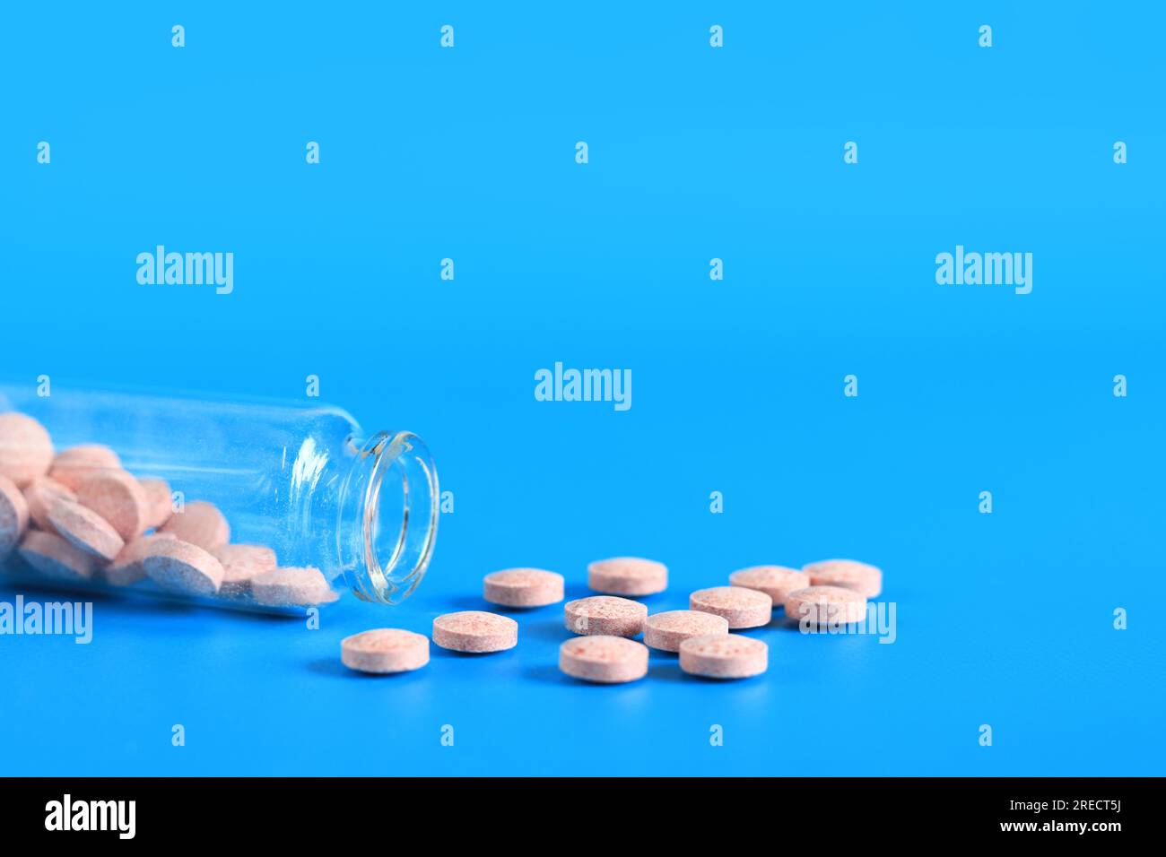 Les pilules roses sont versées dans une bouteille en verre sur un fond bleu. Complexe de vitamine B, espace de copie. Soins de santé, pilules médicales et compléments alimentaires Banque D'Images
