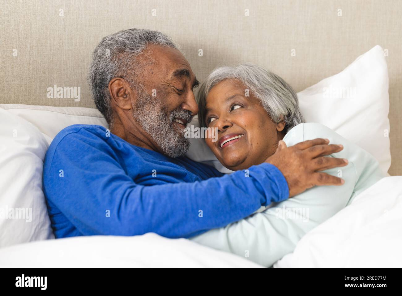Heureux couple biracial senior couché dans le lit et embrassant à la