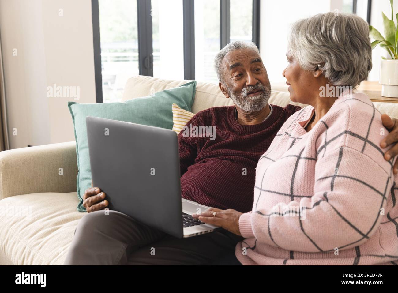 Heureux couple biracial senior assis sur le canapé et utilisant un ordinateur portable à la maison Banque D'Images