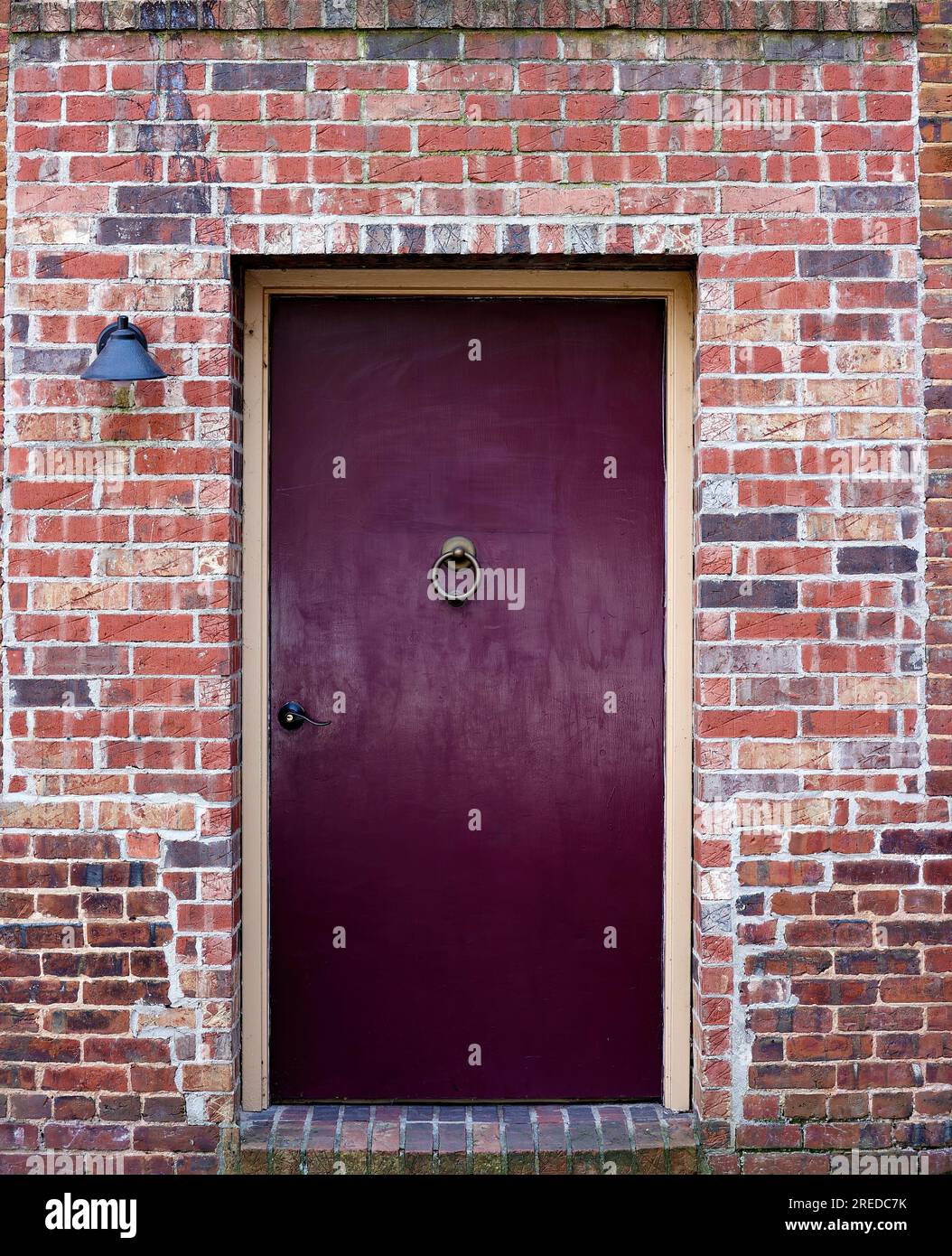 Une porte marron avec un heurtoir en laiton se détache contre le mur extérieur en briques d'un bâtiment. Banque D'Images