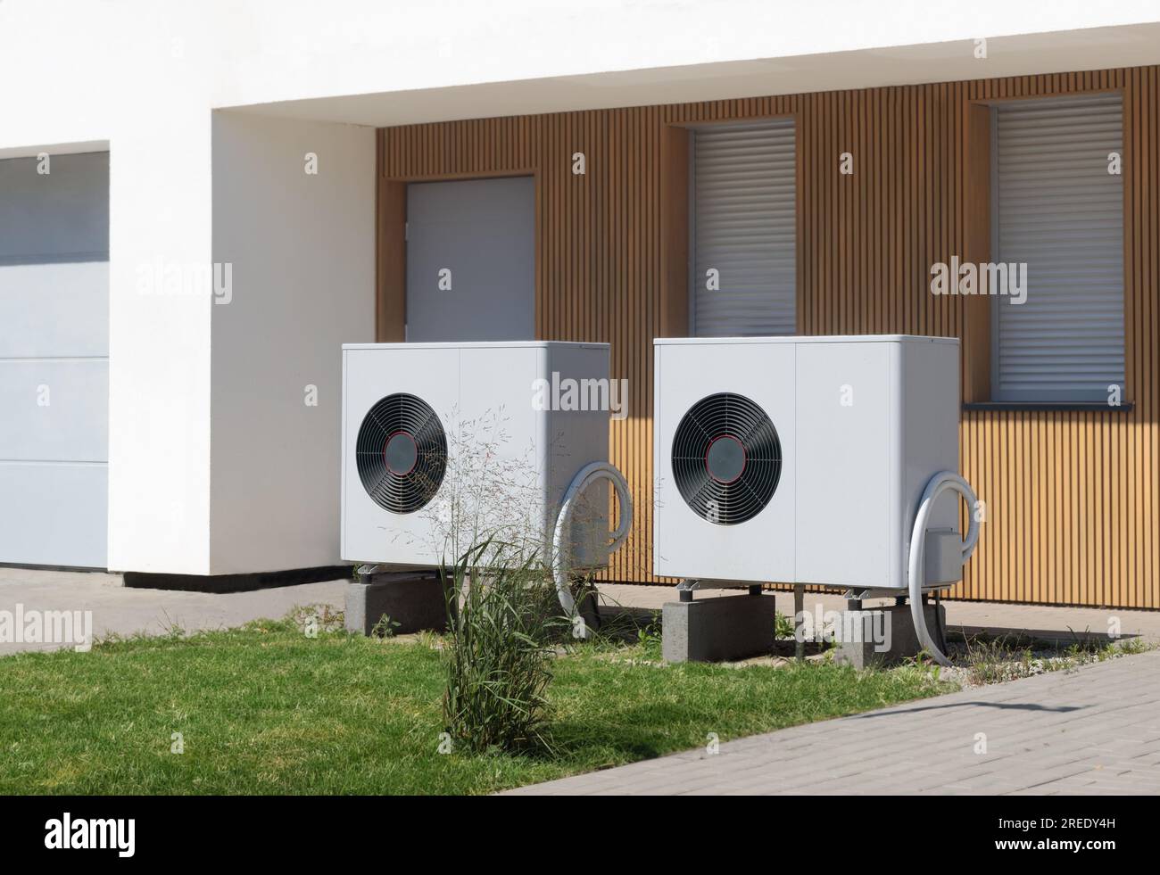Deux pompes à chaleur écologiques situées en face d'une maison moderne avec une pelouse luxuriante, symbolisant des solutions de chauffage vertes. Banque D'Images