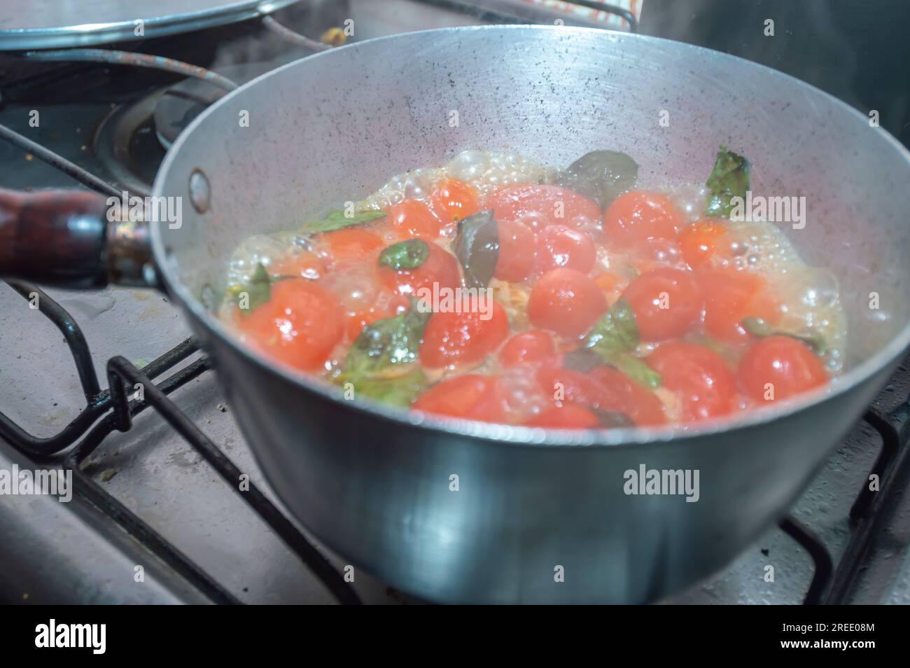 Tomates cerises dans une poêle en cours de cuisson avec mangericão pour faire une sauce tomate naturelle, concept de cuisine italienne. Banque D'Images