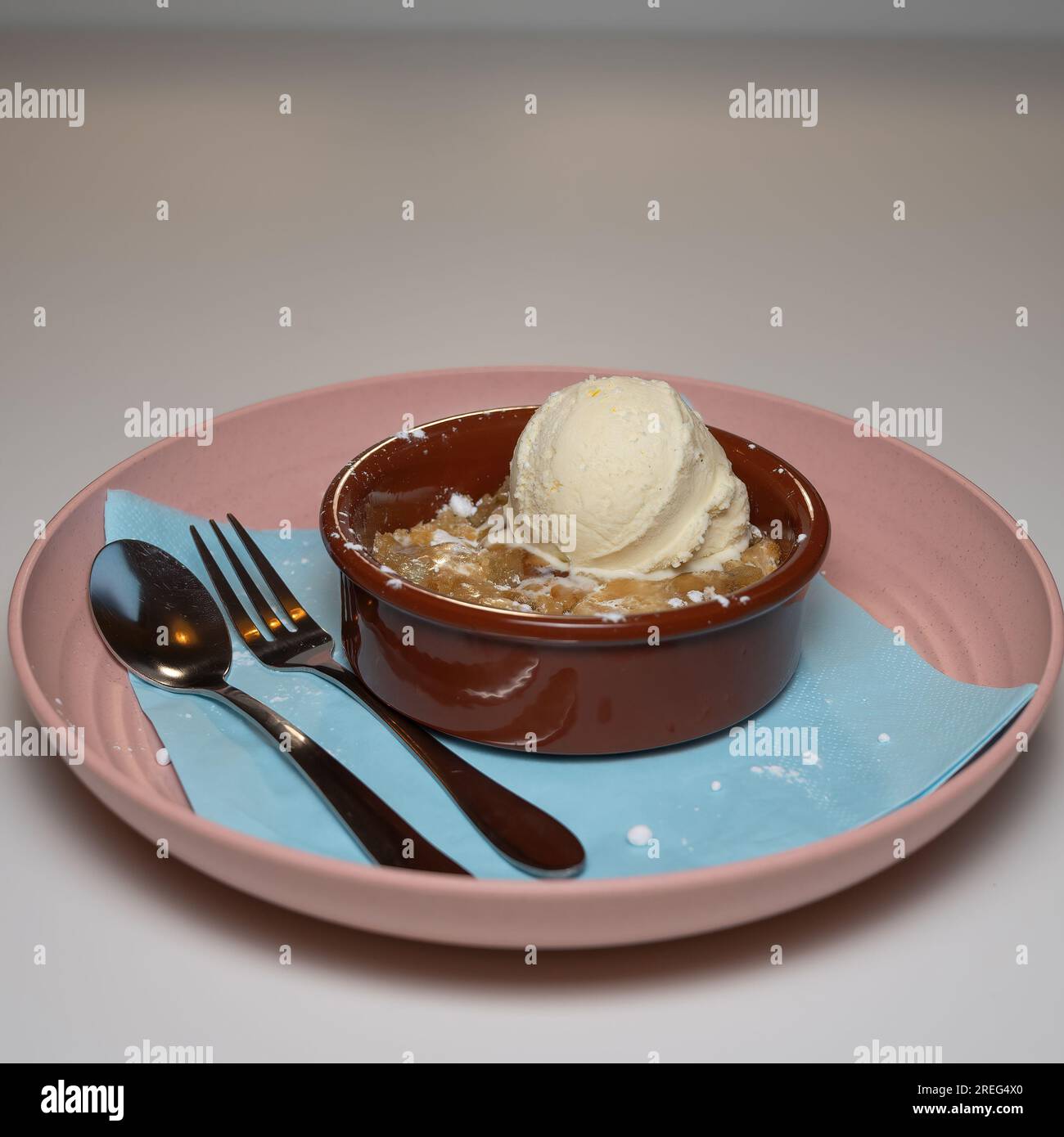une boule de glace à la vanille servie sur une pâte à biscuits chaude servie dans un bol rouge foncé sur une assiette rose. Banque D'Images
