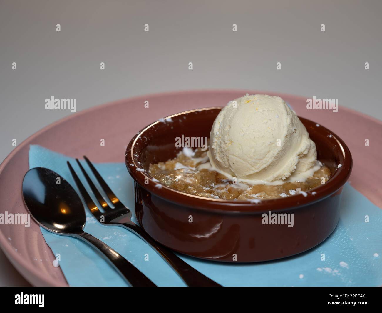 une boule de glace à la vanille servie sur une pâte à biscuits chaude servie dans un bol rouge foncé sur une assiette rose. Banque D'Images