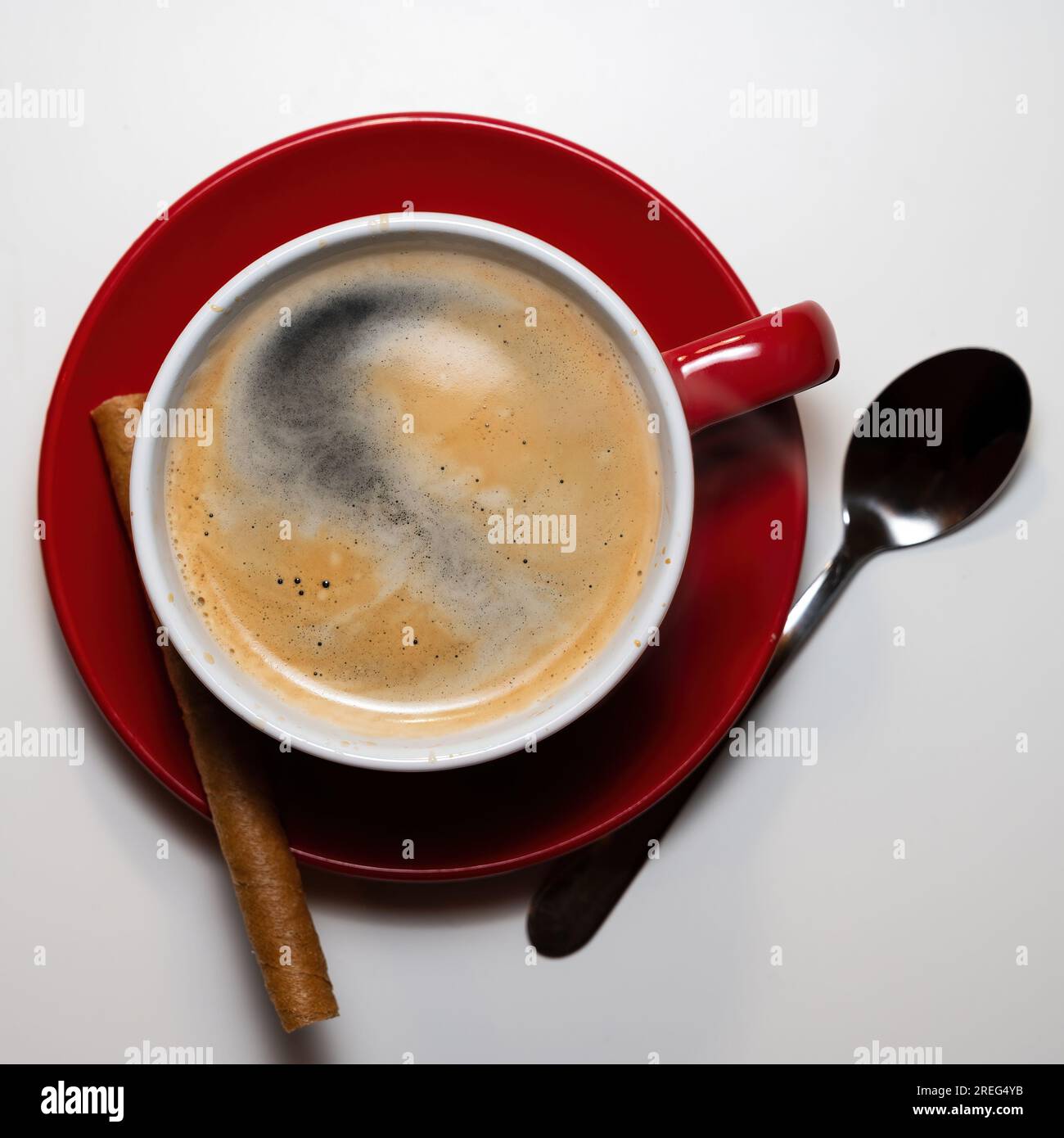 tasse de café servi dans une tasse sur une assiette rouge avec une cuillère en argent et un bâton de cannelle Banque D'Images