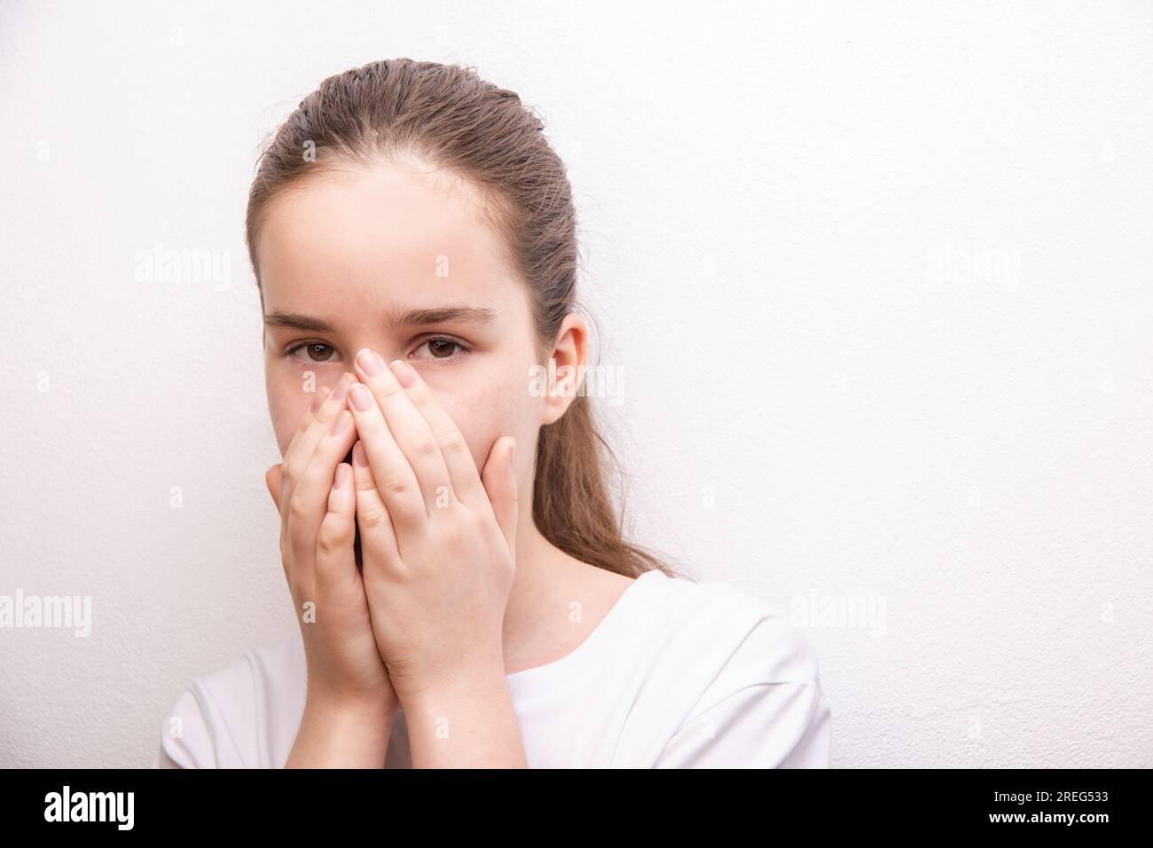 éternuer fille allergique souffre d'allergie, l'adolescent cache la bouche derrière les mains sur la texture de mur de peinture blanche Banque D'Images