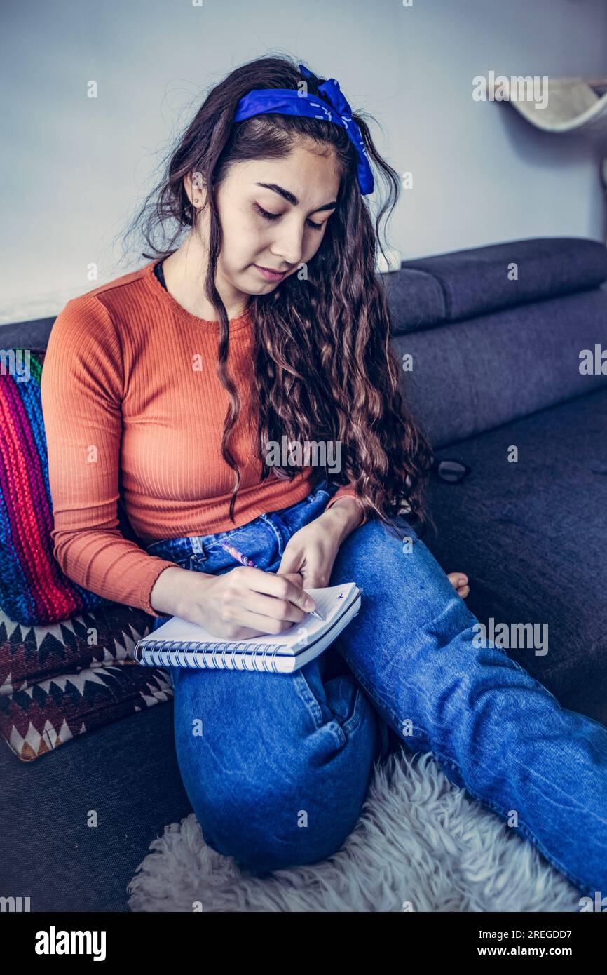 Femme de race mixte concentrée dans l'écriture dans le cahier dans l'intérieur de la maison Banque D'Images