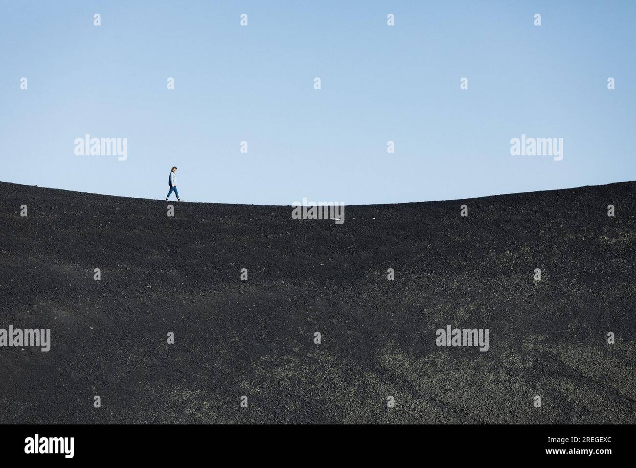 femme marche seule sur une ligne d'horizon concave de sable de basalte noir Banque D'Images