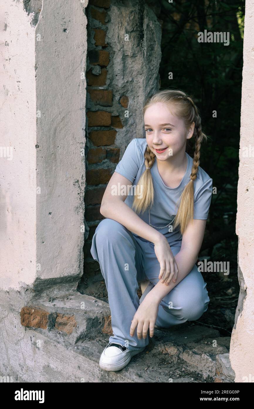 portrait d'une belle fille blonde avec des tresses à un mur de briques. une fille de 13-15 ans est assise dans l'ouverture du mur et regarde la caméra, sm Banque D'Images