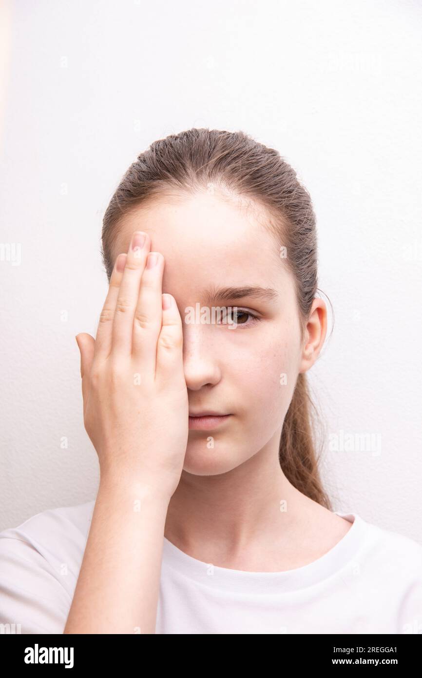 une adolescente test de vision dans une clinique ophtalmologiste. fille couvre un œil avec sa paume sur fond blanc Banque D'Images
