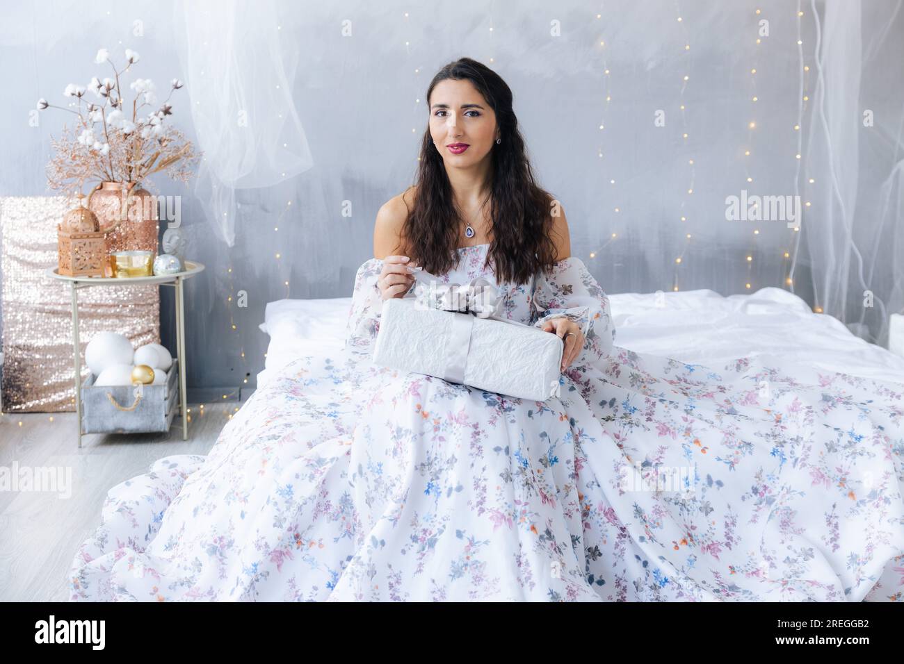 Une fille dans une robe blanche déballe un cadeau Banque D'Images