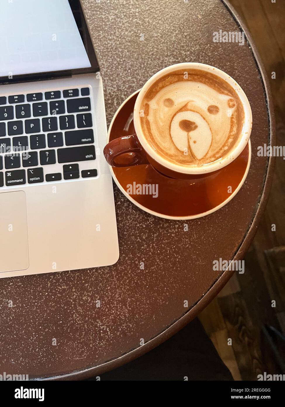 Ordinateur portable et latte avec un ours latte art, travaillant dans un café. Banque D'Images