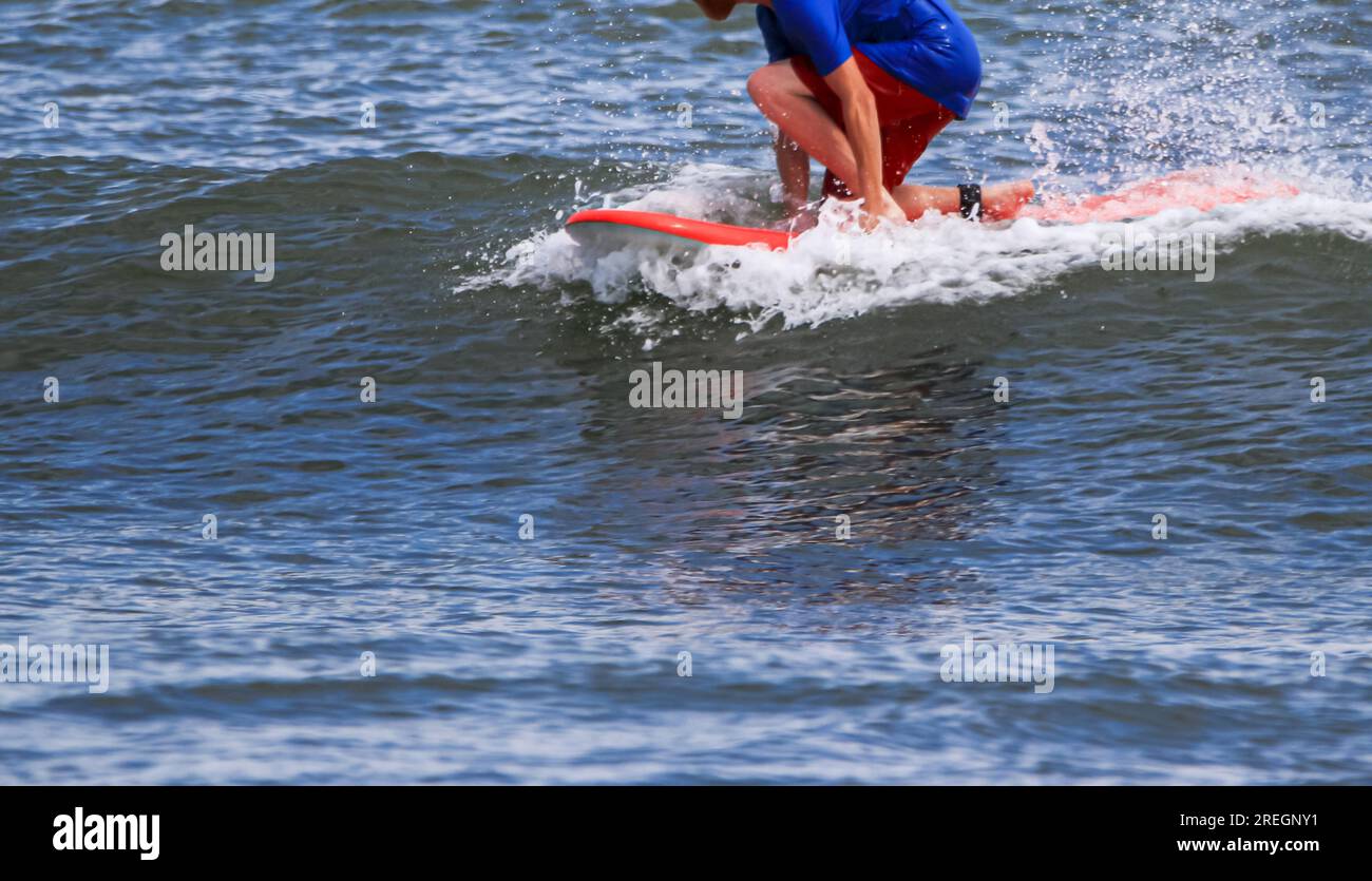 Un surfeur s'accroupissant bas sur un genou, chevauchant sur le sommet d'une petite vague tout en surfant à Gilgo Beach long Island. Banque D'Images
