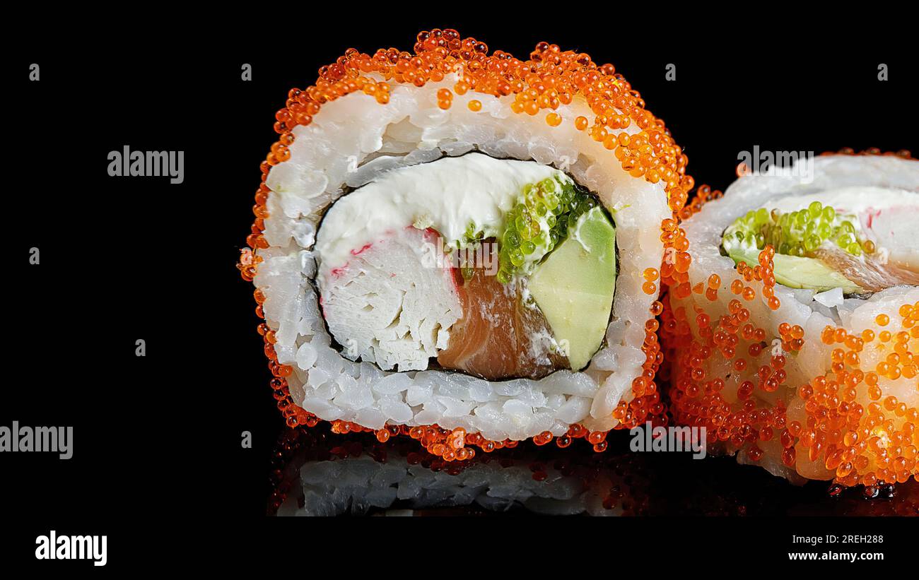 Roul de sushi au saumon, fromage à la crème, crabe, avocat et caviar tobiko, sur un miroir noir Banque D'Images