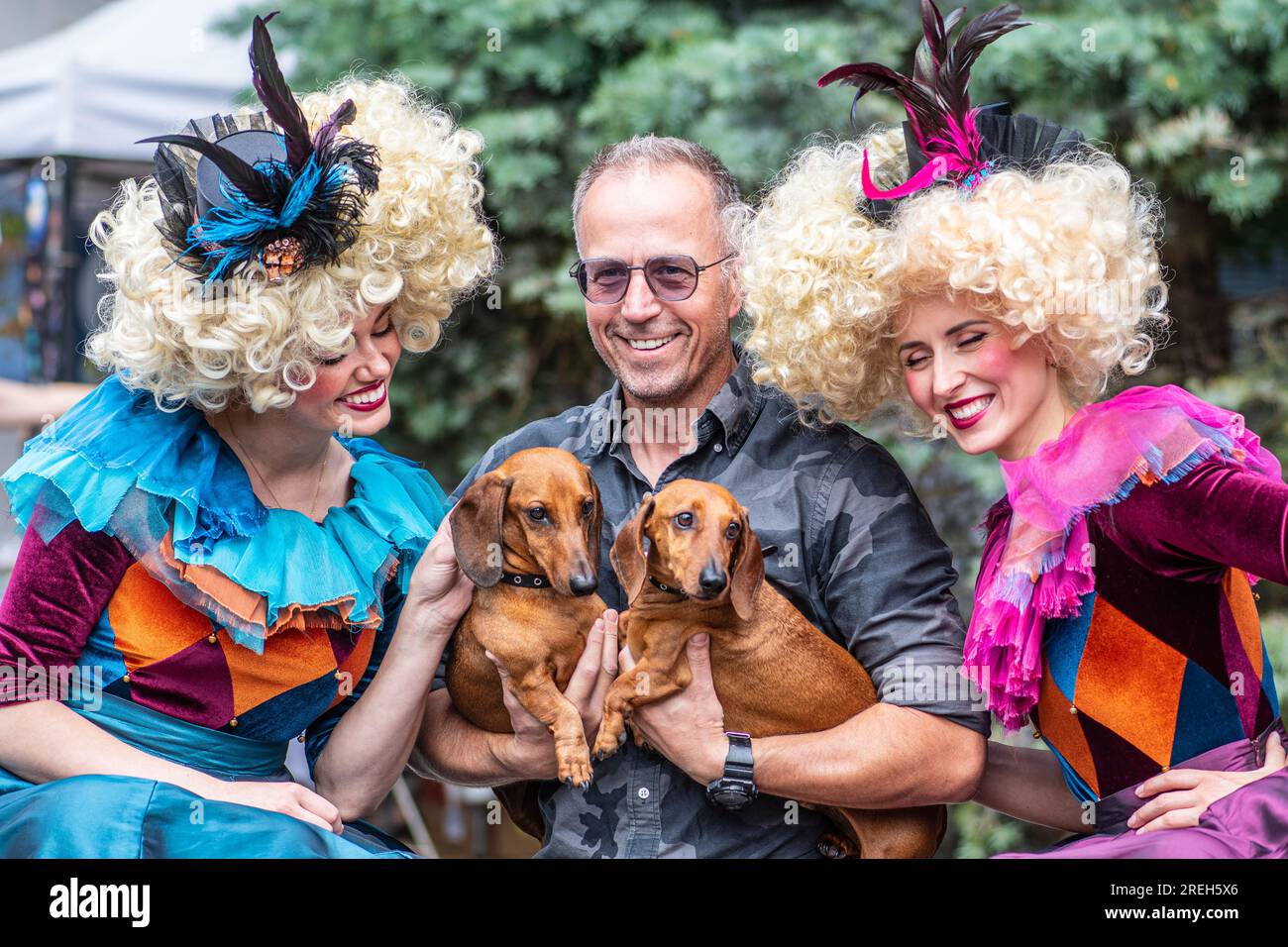 Beau couple de filles dans des vêtements colorés vintage et des perruques prenant la photo avec un homme et ses deux chiens de teckel pendant le festival national letton Banque D'Images