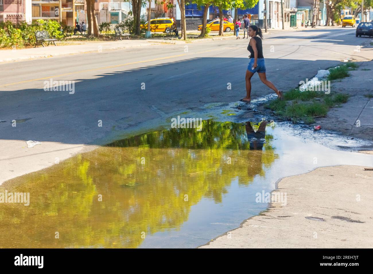 La Havane, Cuba, Une jeune cubaine traverse une rue vide de la ville. Il y a une grande flaque d'eau sale stagnante près du trottoir. Banque D'Images