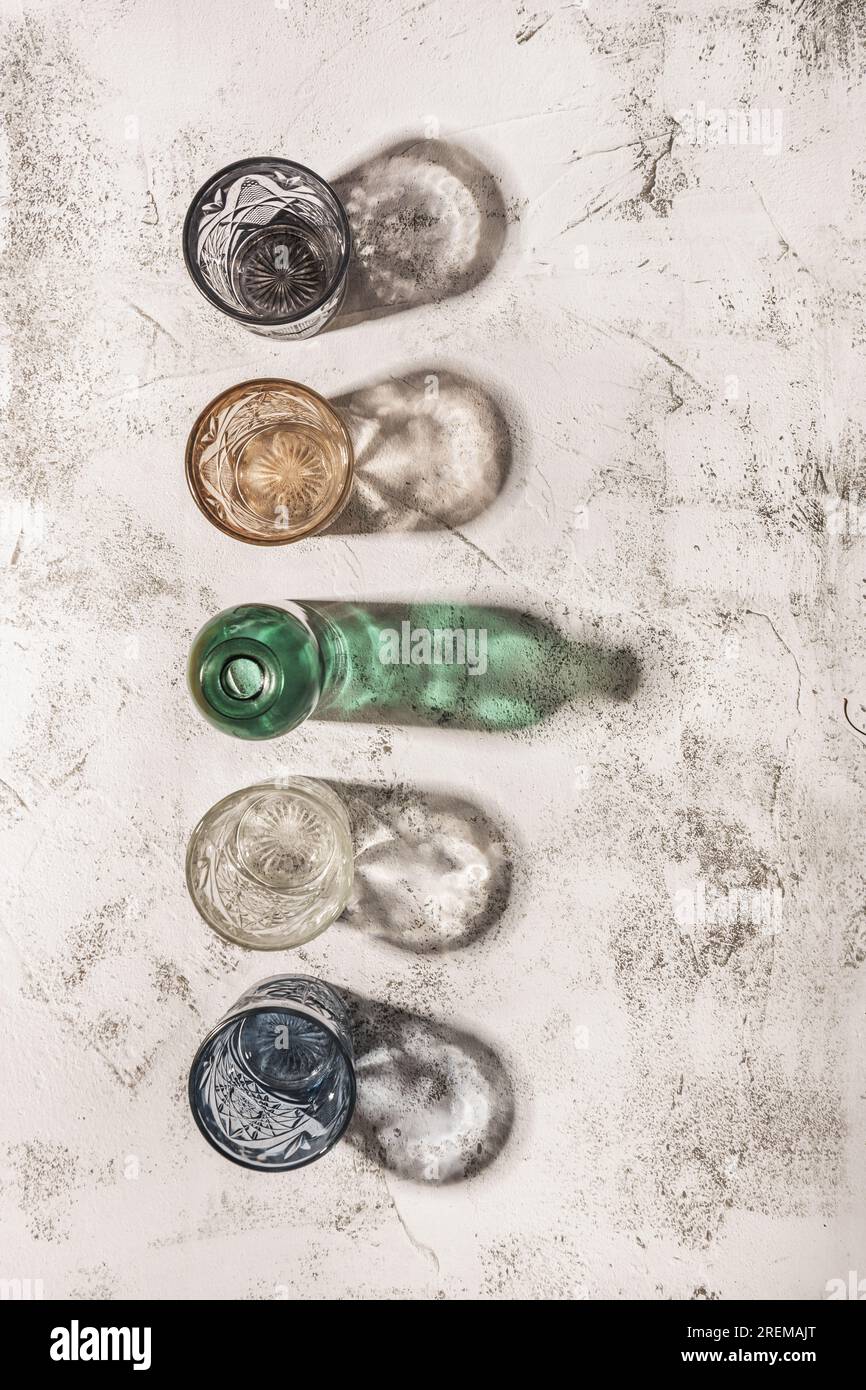 Certains verres en cristal colorés faisant de l'ombre sur une surface rugueuse blanche et grise Banque D'Images