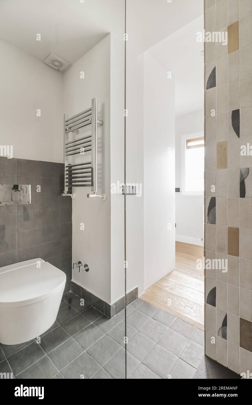 Les murs d'une salle de bains carrelée avec des carreaux décoratifs modernes, une toilette suspendue au mur, des carreaux carrés sur les sols et les murs et un porte-serviettes chauffant chromé Banque D'Images
