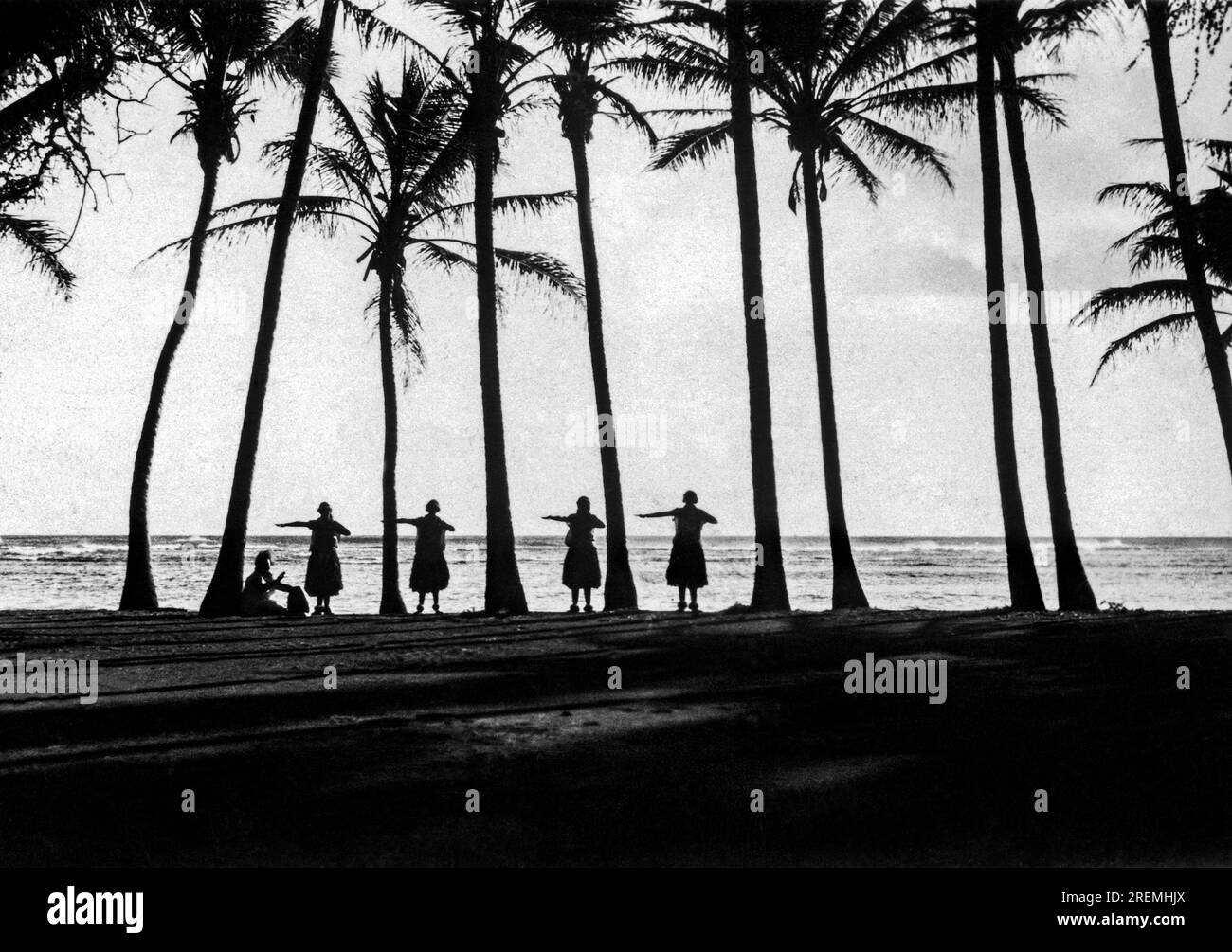 Hawaii : c. 1922 danse folklorique à Hawaii. Les indigènes à susnset font la danse hula-hula sous les palmiers au bord de l'eau. Banque D'Images