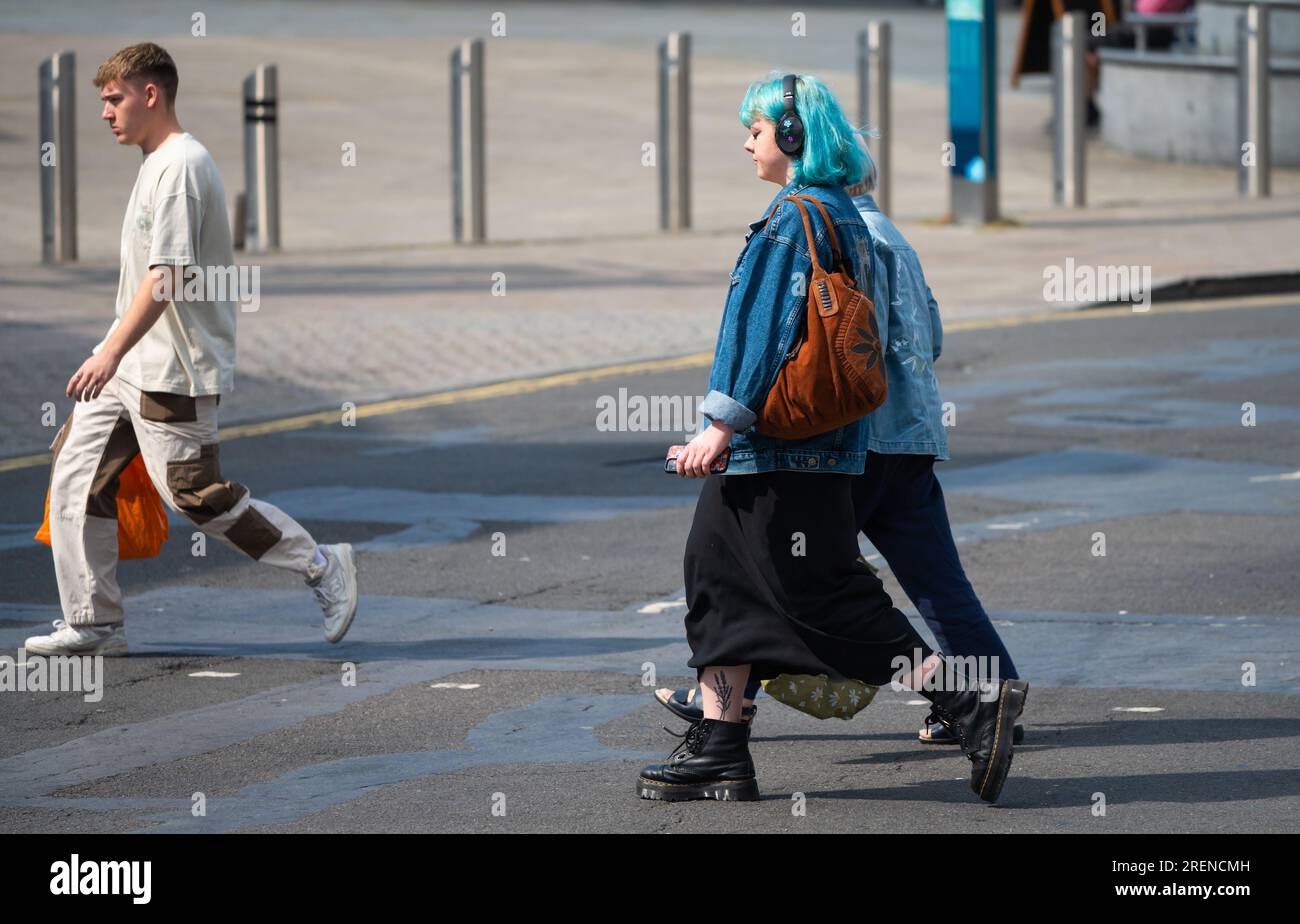 Jeune femme habillée à la mode, tendance, avec les cheveux verts portant des écouteurs marchant à travers une route à Brighton & Hove, Royaume-Uni. Banque D'Images