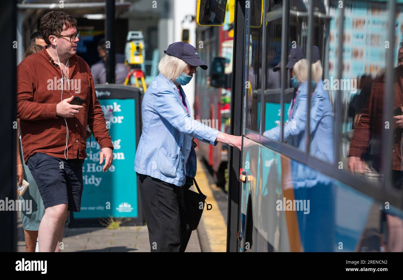 Dame portant un masque facial embarquant dans un bus au Royaume-Uni. Banque D'Images
