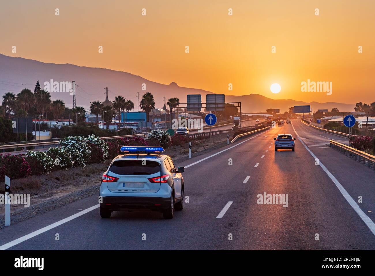 Voiture de police de la circulation conduisant sur une autoroute avec le soleil tôt le matin se levant sur les montagnes. Banque D'Images